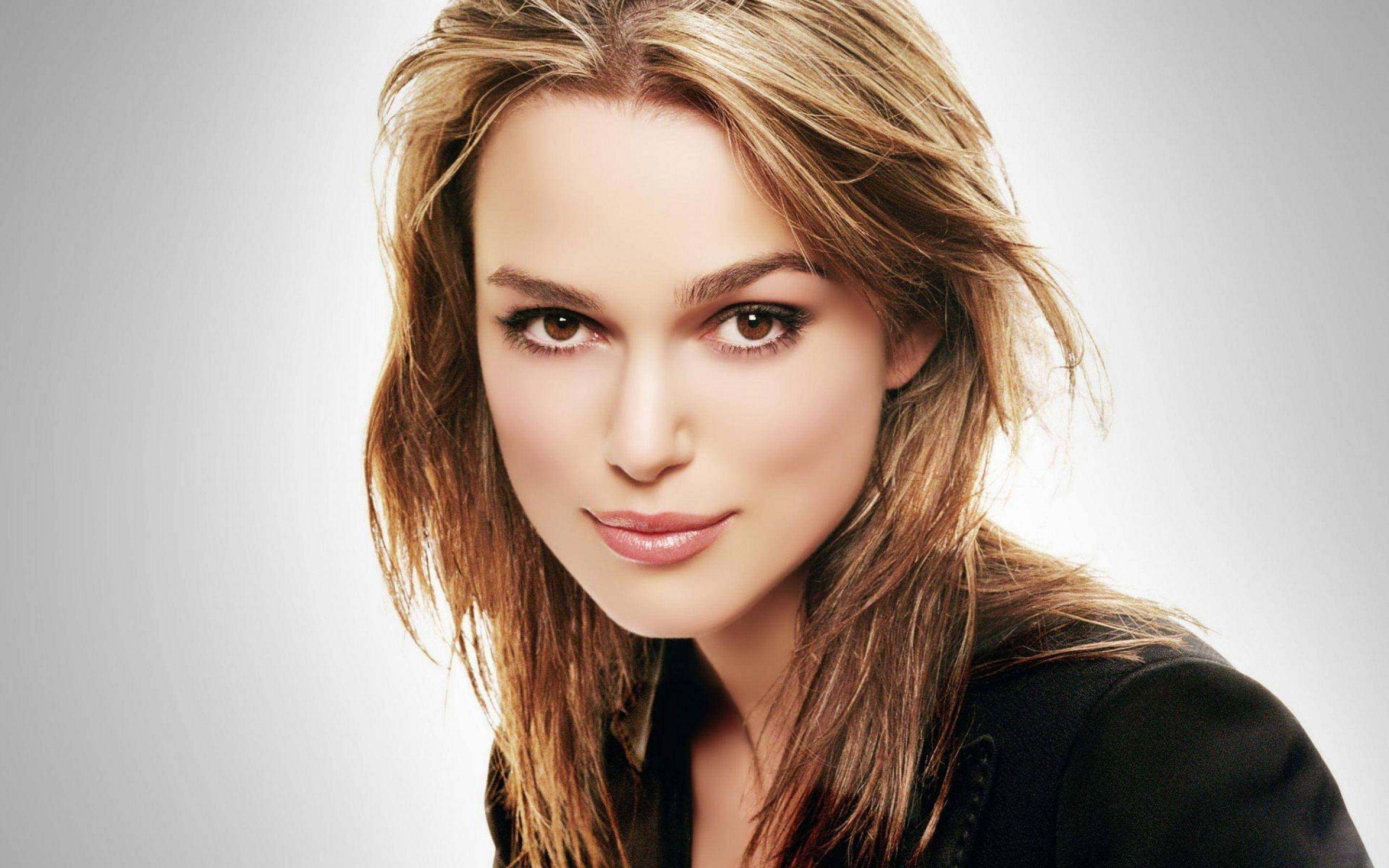 Keira Knightley 桌布 壁紙 — 一位金棕色頭髮、眼神強烈的女性的特寫肖像，背景為柔和的灰色。
