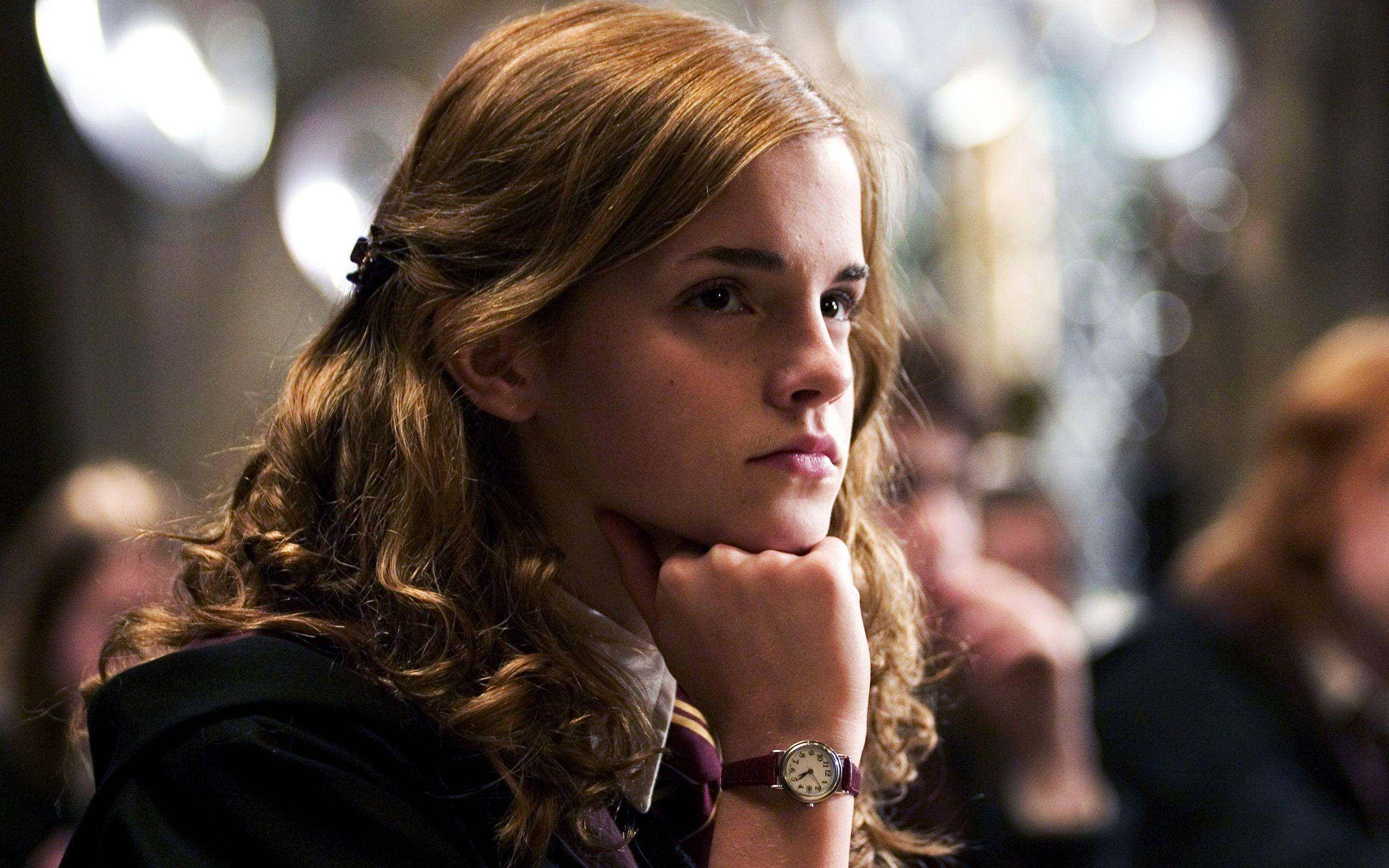 Hermione 桌布 壁紙 — 一位金色捲髮的年輕女子將下巴擱在手上，在昏暗的房間裡若有所思地凝視著，身後有柔和的散景燈光。