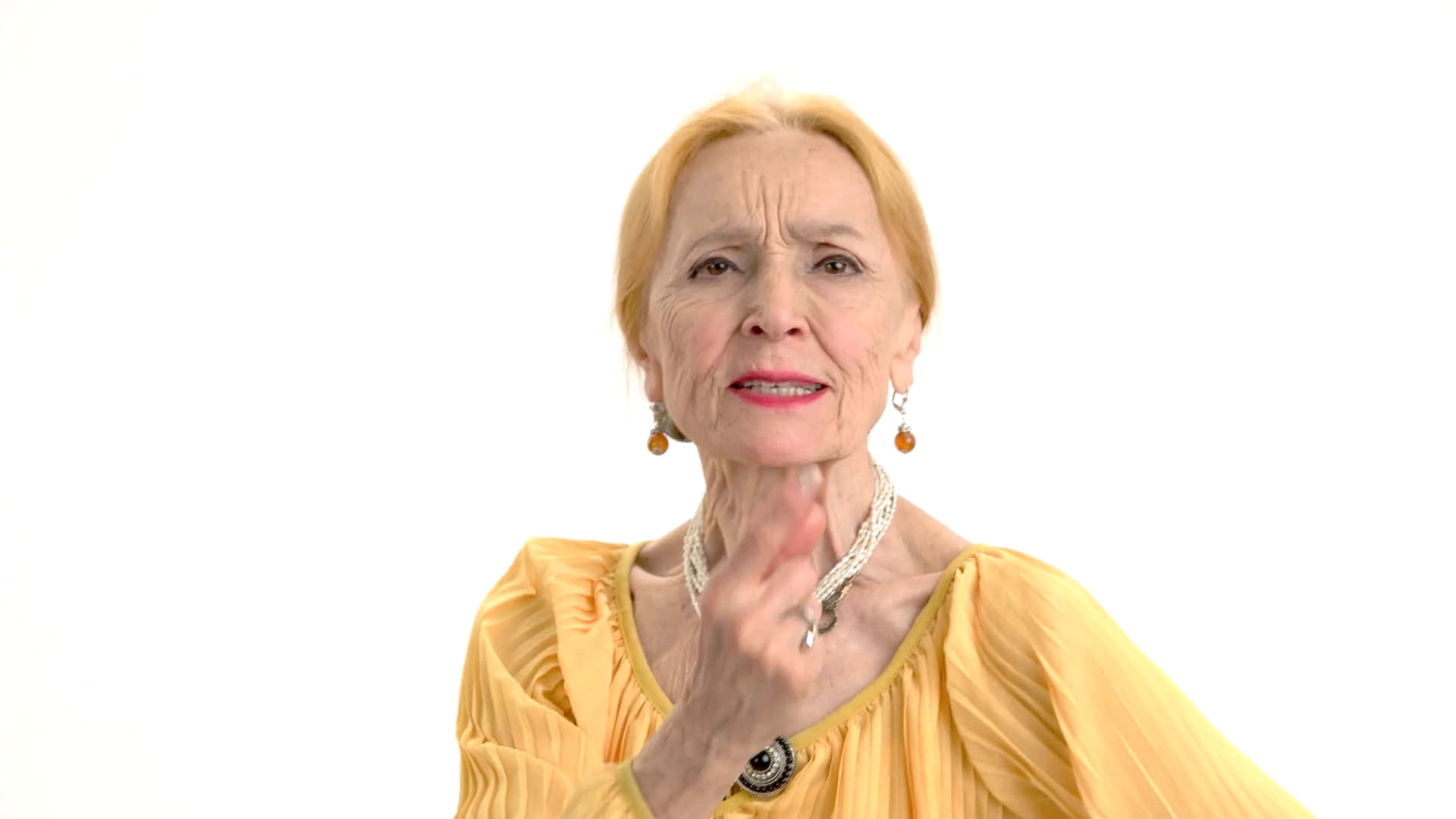 Old Lady 桌布 壁紙 — 一位金髮、身穿黃色上衣的老年女性，在純白背景前輕輕觸碰下巴。