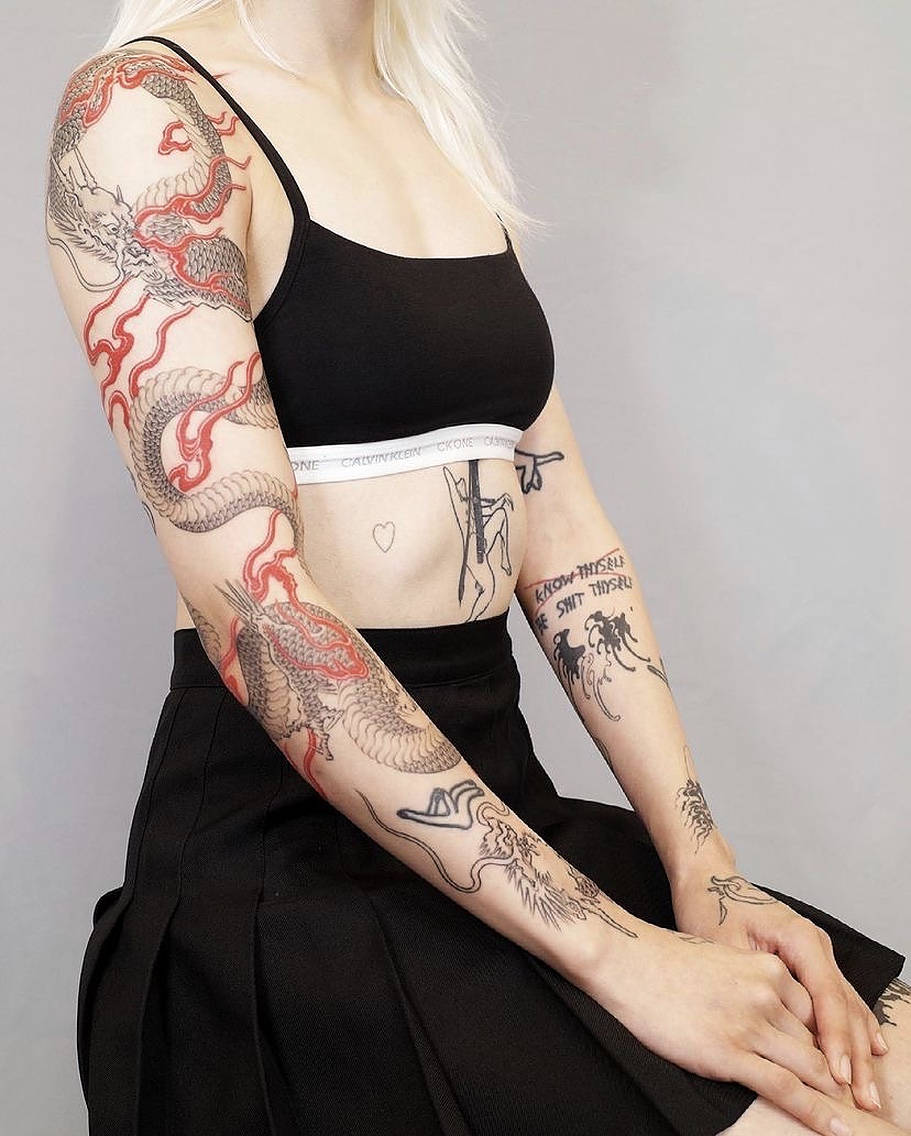 Japanese Dragon Tattoo 桌布 壁紙 — 一位金髮人士在純灰色背景前展示覆蓋其手臂和軀幹的複雜黑紅龍紋身。