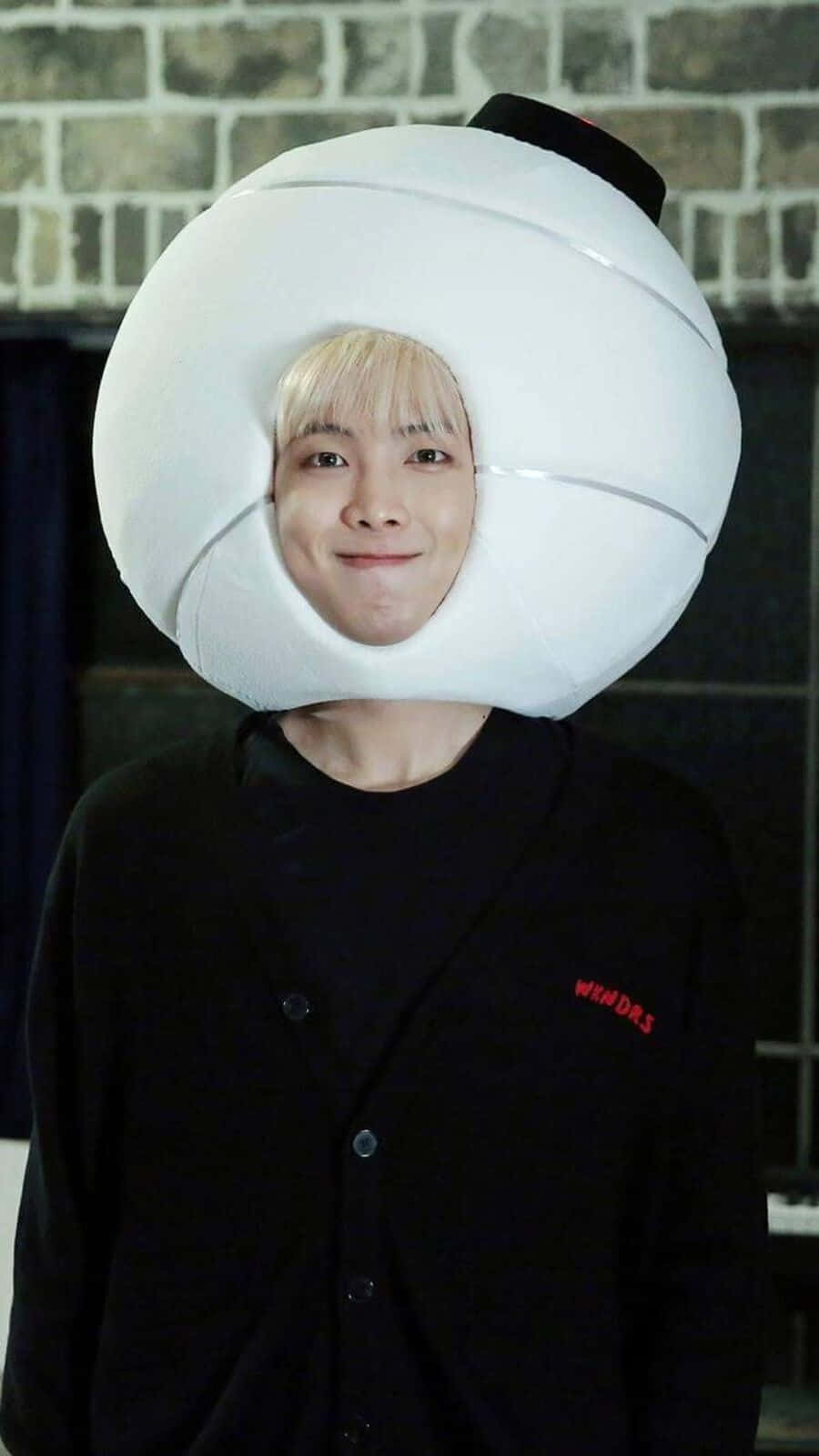 Bts Army Bomb 桌布 壁紙 — 一位金髮人士穿著大型白色充氣餃子服裝，在磚牆前微笑。