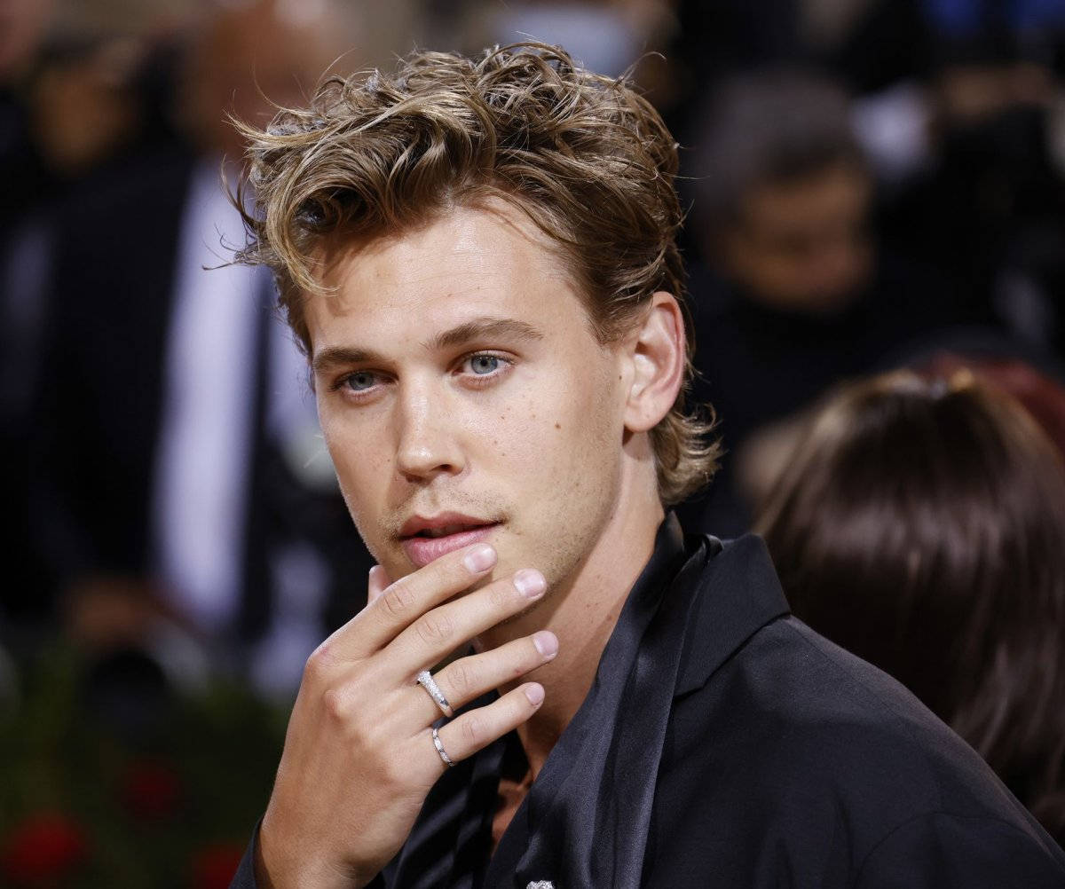 Celebrity 桌布 壁紙 — 一位金髮凌亂、藍眼睛的年輕男子的特寫肖像，身穿黑色西裝，用戴著戒指的手觸摸下巴。