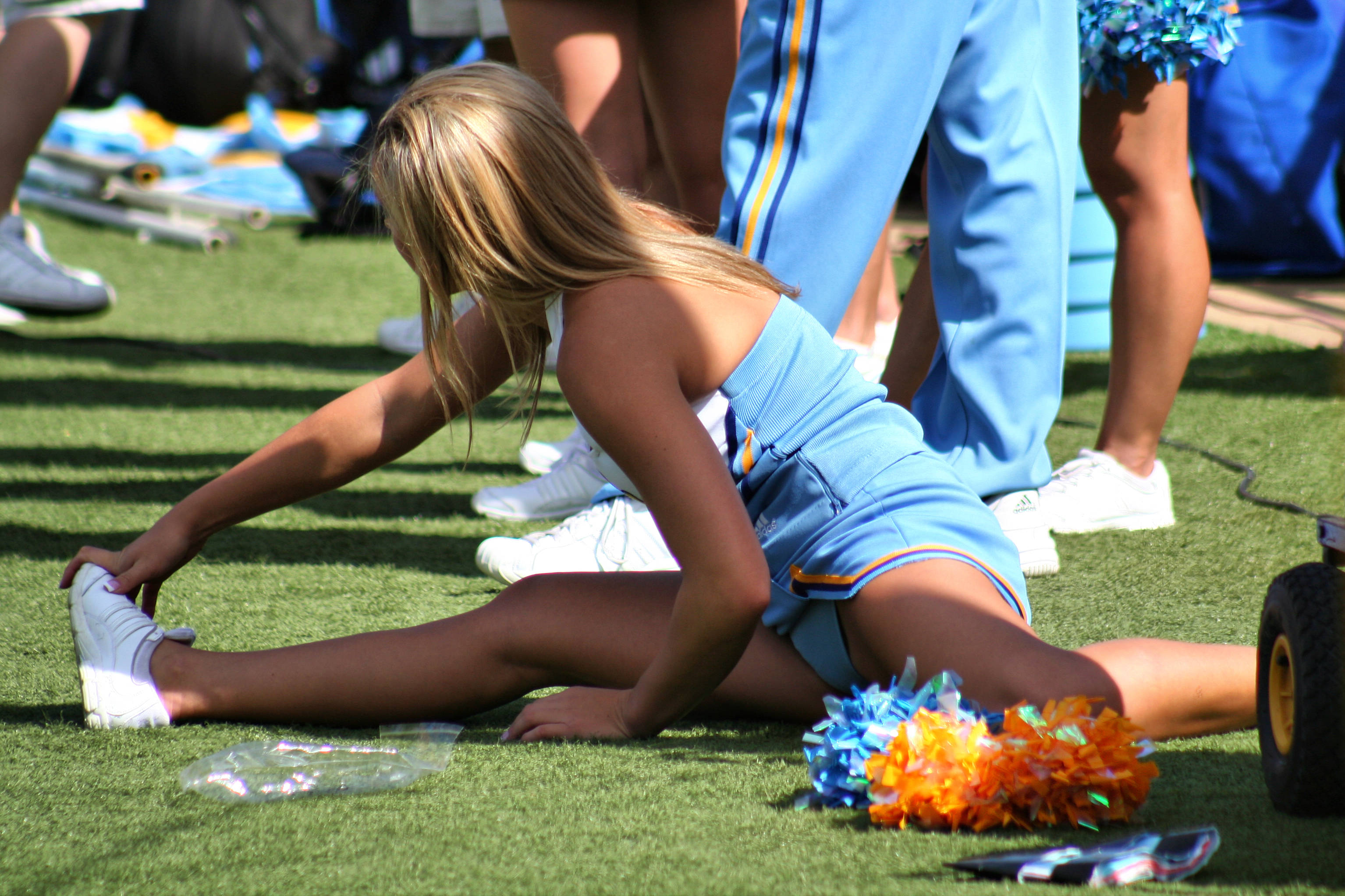 Cheerleader 桌布 壁紙 — 一位金髮啦啦隊員身穿藍色制服，在綠色草地上伸展，旁邊有彩球和水瓶。