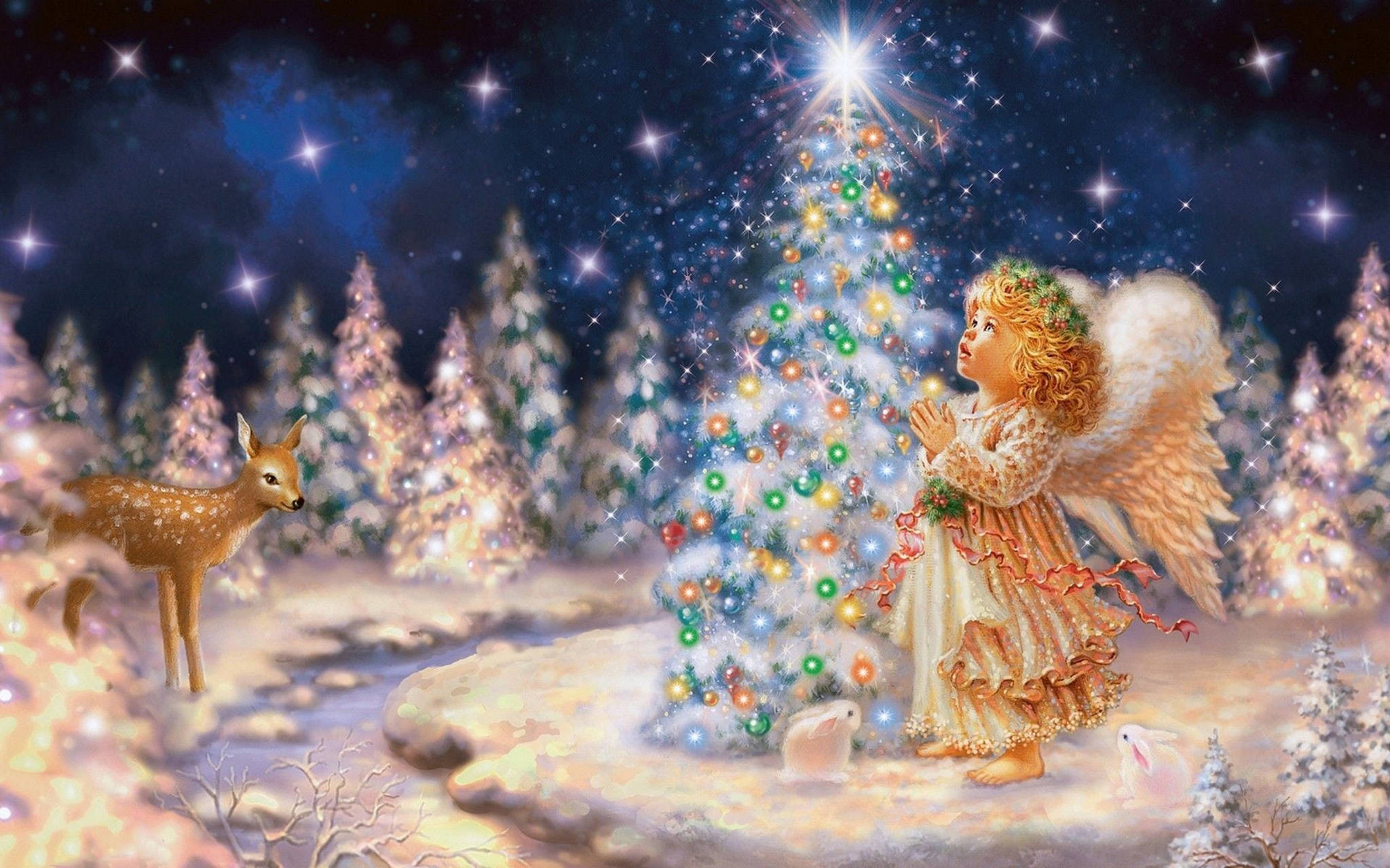 angels 桌布 壁紙 — 一位金髮天使身穿飄逸長袍，跪在閃爍的聖誕樹旁，背景是星光閃爍的冬夜天空，附近有一隻鹿在觀看。