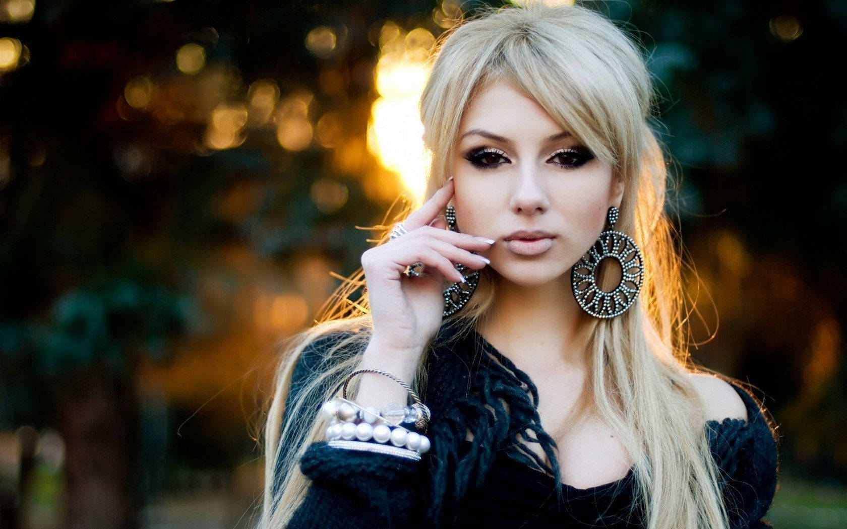 Blonde Woman 桌布 壁紙 — 一位金髮女子化著誇張妝容，戴著大耳環，在戶外擺姿勢，金色陽光穿過她身後的樹木灑落下來。