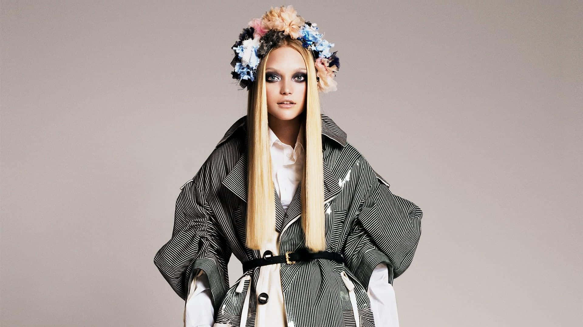 Gemma Ward 桌布 壁紙 — 一位金髮女子化著誇張的妝容，穿著條紋外套，戴著色彩繽紛的花冠，背景是純灰色。