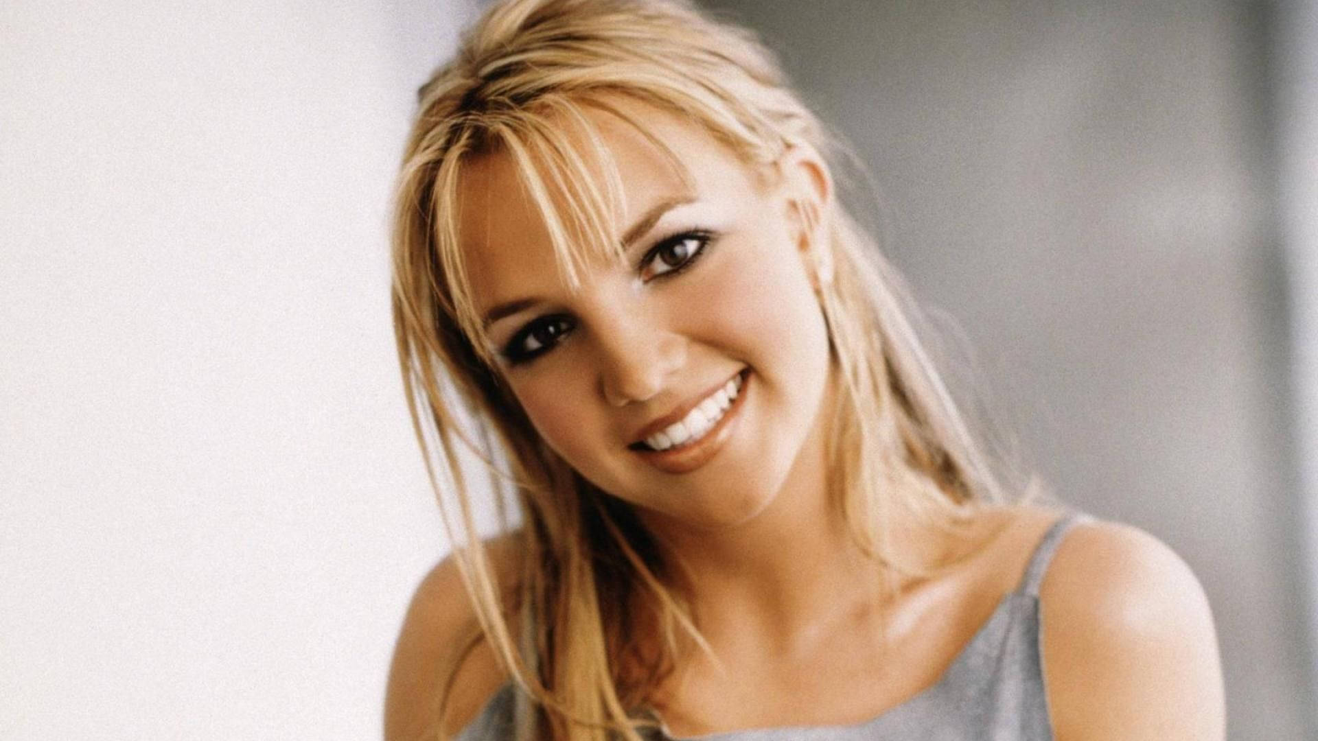 britney 桌布 壁紙 — 一位金髮女子在柔和光線和純色背景下燦爛微笑。