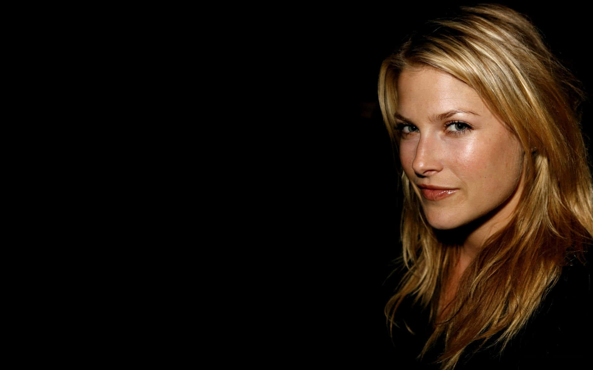 ali larter 桌布 壁紙 — 一位金髮女子在柔和燈光下，對著純黑背景平靜地凝視。