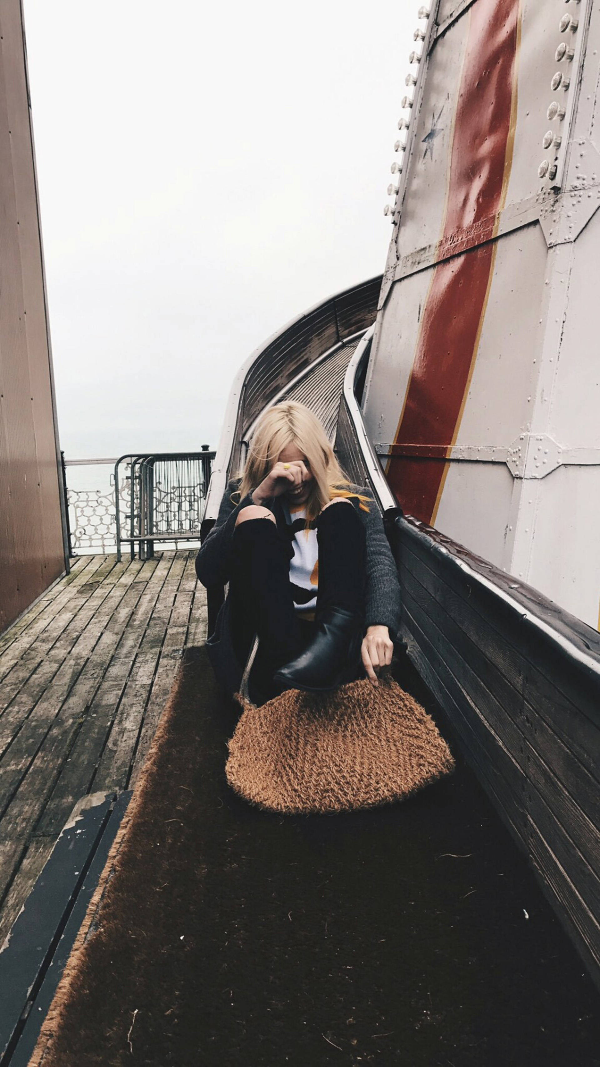 桌布 壁紙 — 一位金髮女子坐在木甲板上，旁邊有一個彎曲的金屬結構，雙手捧著臉。
