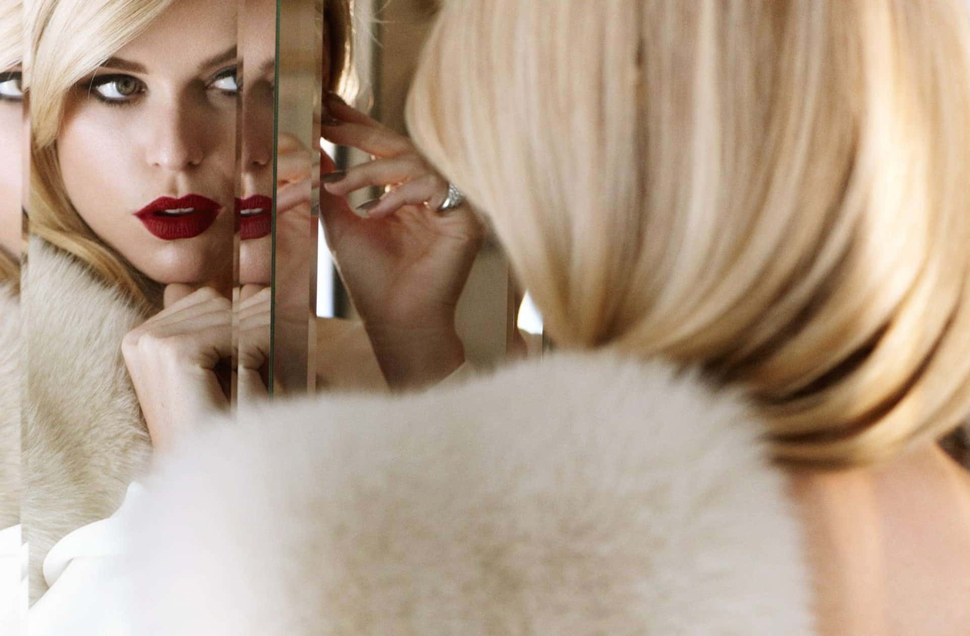 alice eve 桌布 壁紙 — 一位金髮女子塗著大膽的紅唇，穿著蓬鬆的白色毛領，專注地凝視著自己破碎的鏡中倒影。