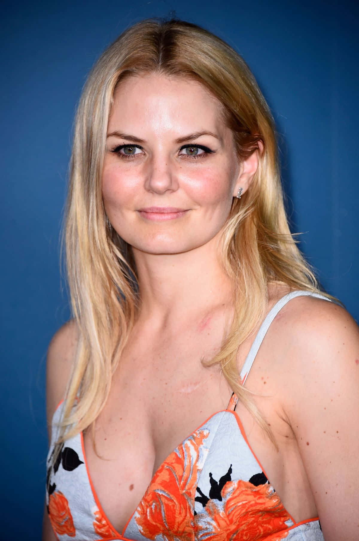 jennifer morrison 桌布 壁紙 — 一位金髮女子帶著溫柔的微笑，身穿花卉圖案上衣，背景是純藍色攝影棚。