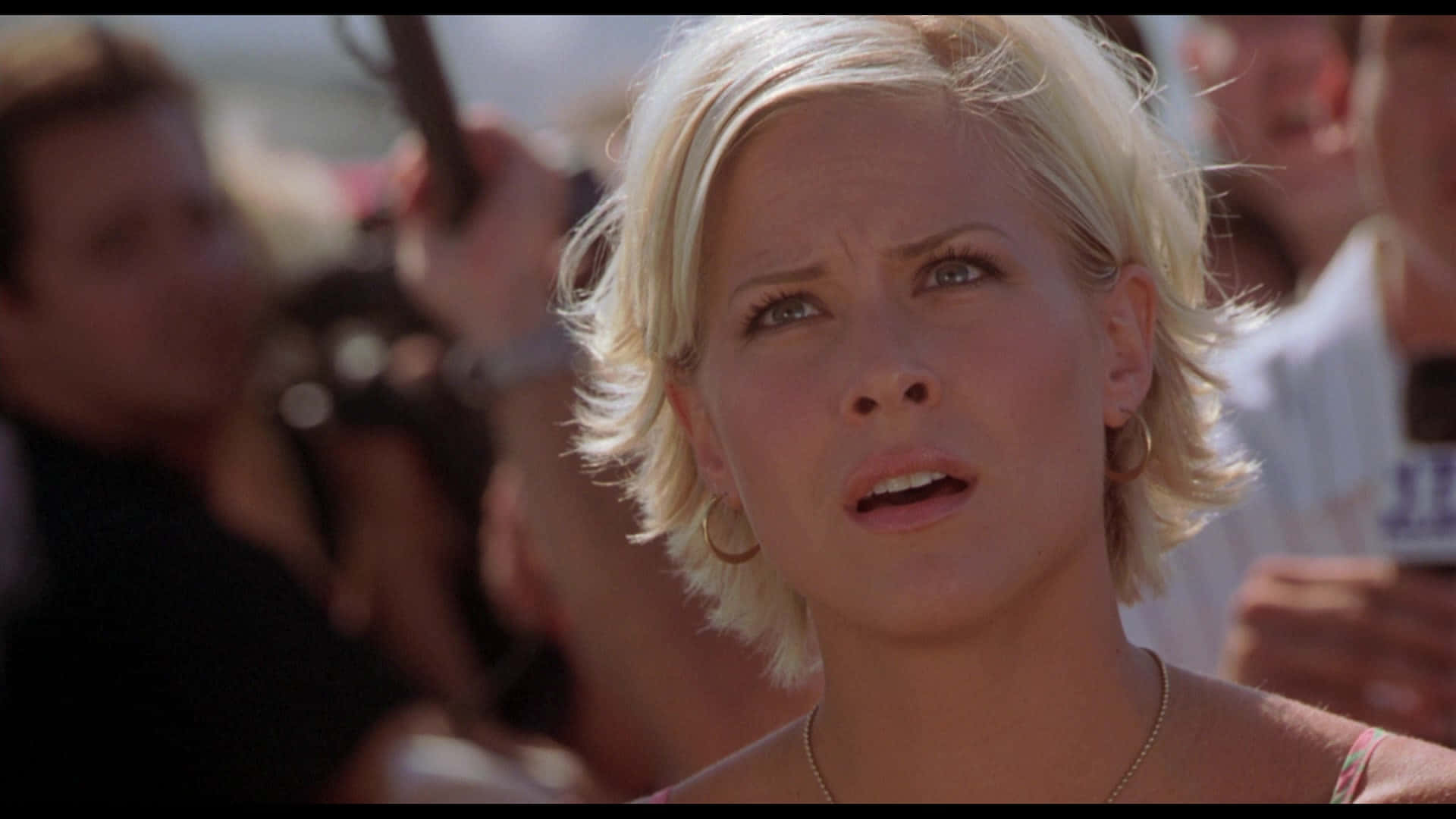 Brittany Daniel 桌布 壁紙 — 一位金髮女子帶著震驚的表情向上看，周圍人群在明亮的日光下包圍著她。