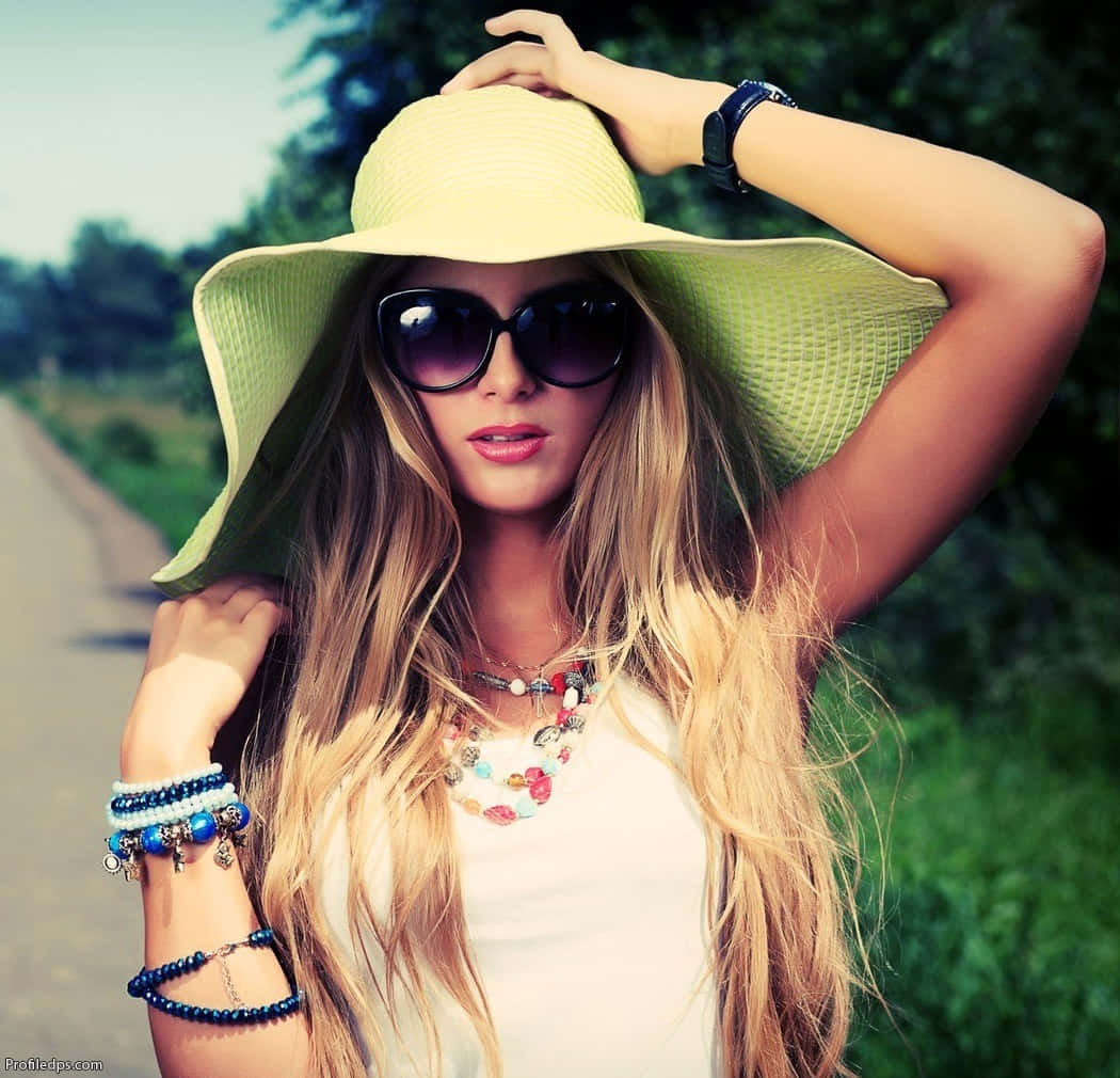 Sunglasses 桌布 壁紙 — 一位金髮女子戴著寬邊綠色帽子和太陽眼鏡，在陽光明媚的日子裡於戶外擺姿勢，身後是茂密的綠植。