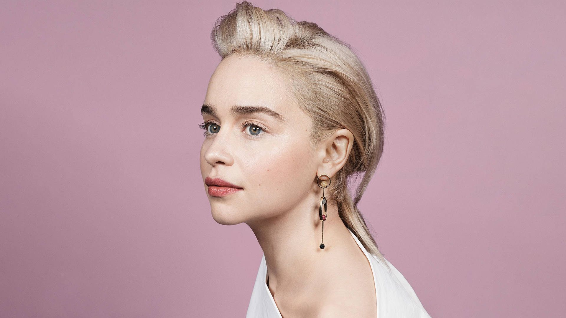 Emilia 桌布 壁紙 — 一位金髮女子戴著引人注目的耳環，在柔和的粉紅色工作室背景下若有所思地凝視。