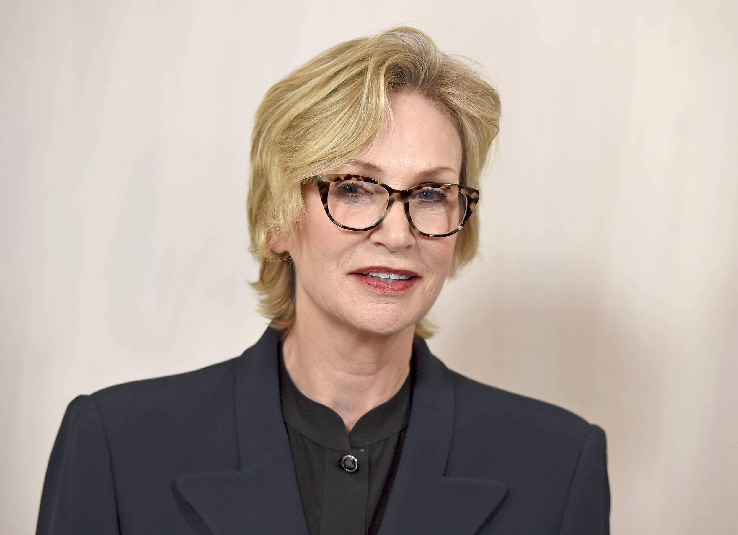 Celebrity 桌布 壁紙 — 一位金髮女子戴著玳瑁眼鏡，身穿深色西裝外套，背景簡潔。