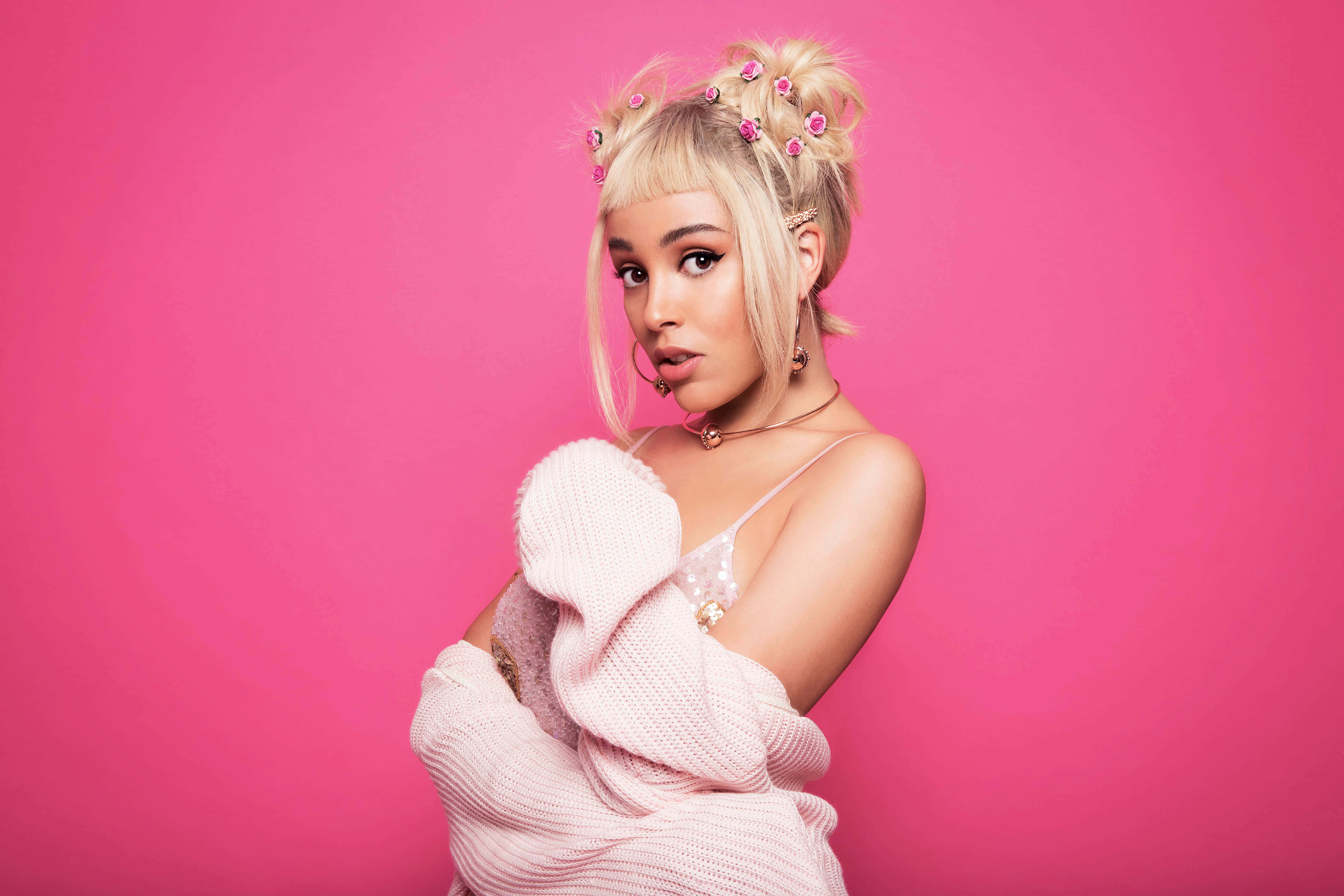 Doja Cat 桌布 壁紙 — 一位金髮女子戴著粉紅色花卉髮飾，穿著舒適的粉紅色毛衣，在充滿活力的粉紅色攝影棚背景前自信地擺姿勢。