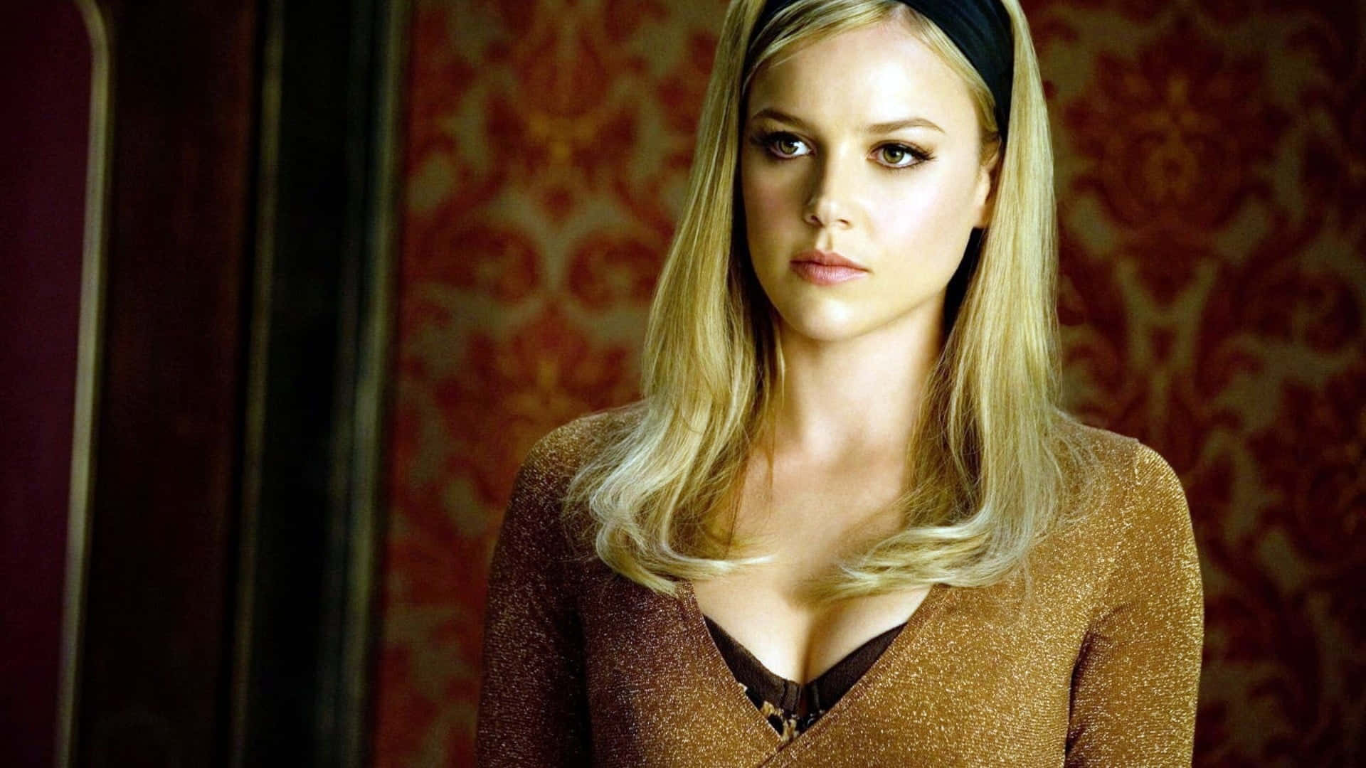 Abbie Cornish 桌布 壁紙 — 一位金髮女子戴著黑色頭帶，對著華麗的紅色錦緞壁紙背景凝視。
