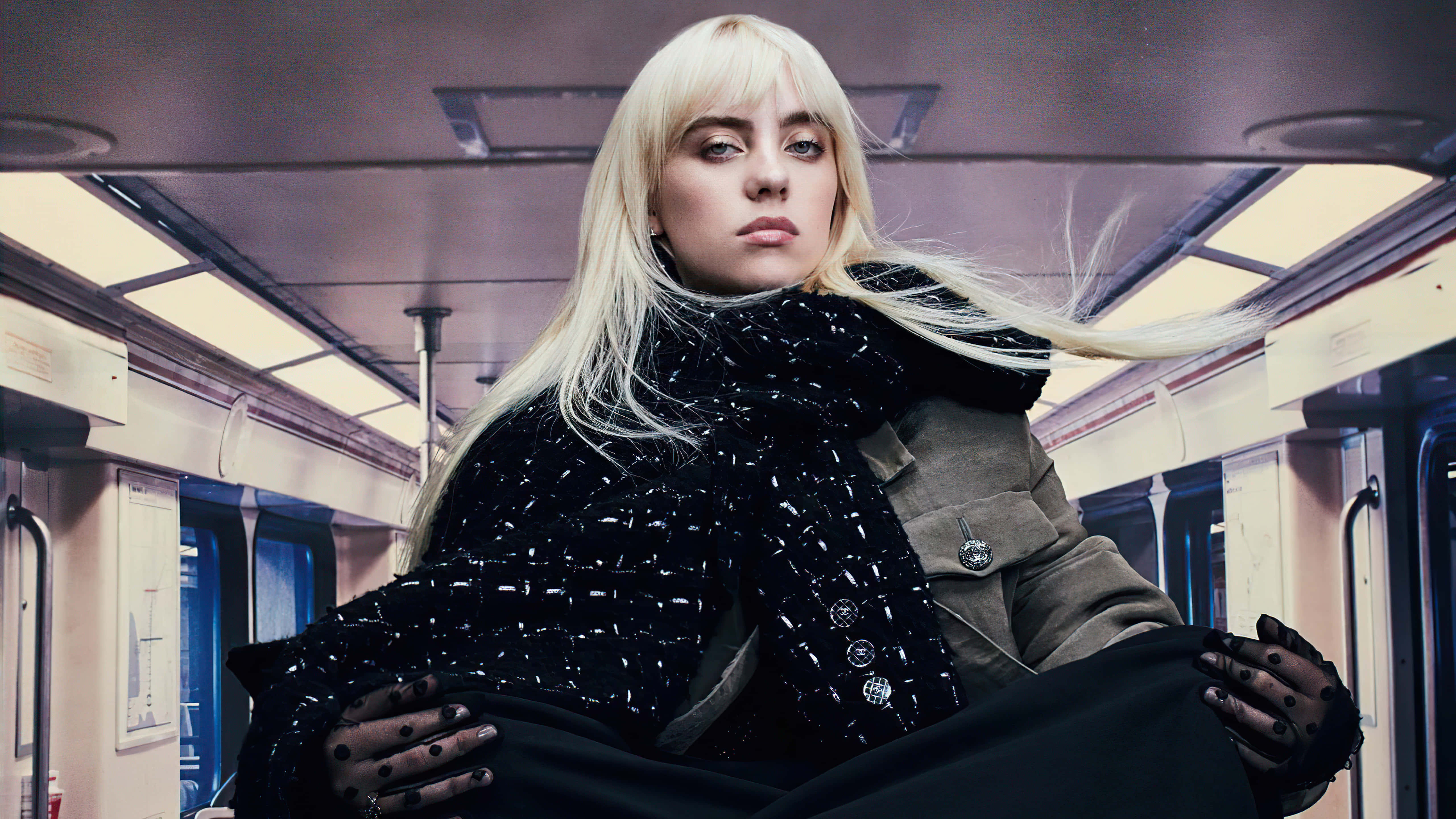 Billie Eilish 2021 桌布 壁紙 — 一位金髮女子眼神專注，自信地坐在地鐵車廂內，身穿黑色紋理外套及手套。