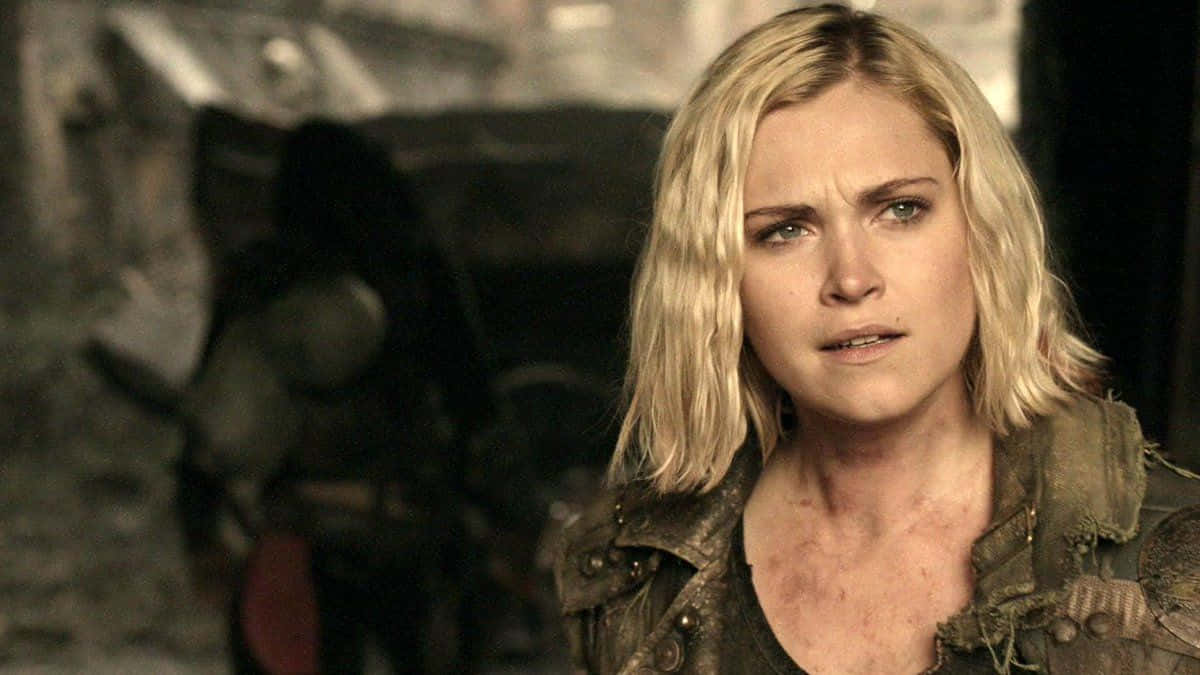 eliza taylor 桌布 壁紙 — 一位金髮女子穿著破舊的夾克，在昏暗骯髒的環境中，帶著緊張的表情專注地凝視。