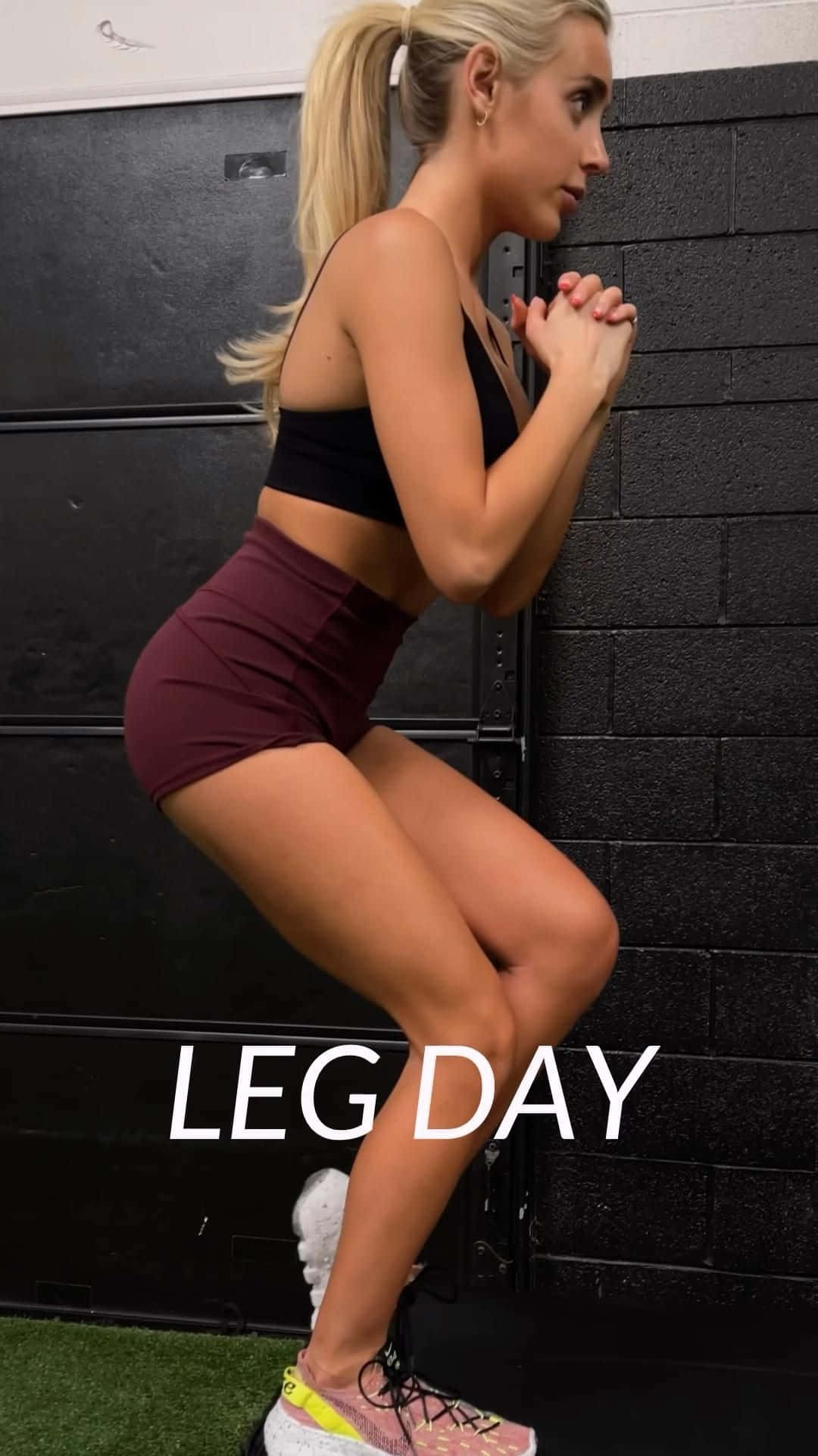 Exercise 桌布 壁紙 — 一位金髮女子穿著運動服，在黑色磚牆前做深蹲，牆上有『LEG DAY』字樣。