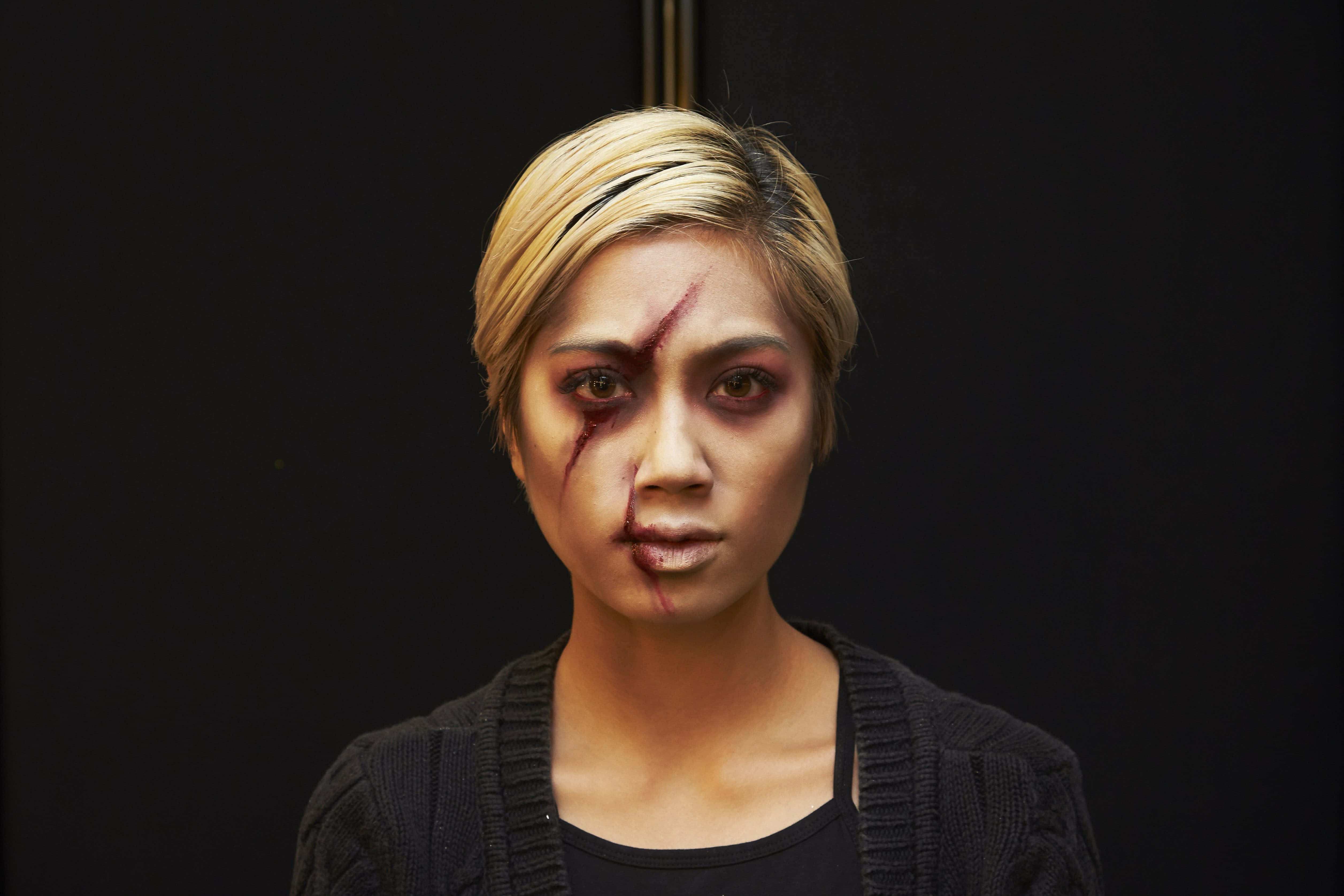 Halloween Makeup 桌布 壁紙 — 一位金髮女子臉上帶有血痕，在黑色背景下強烈凝視。