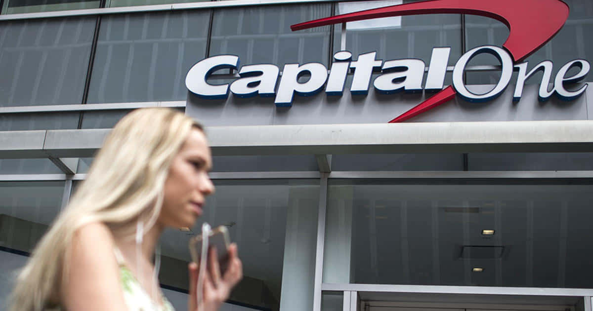 Bank 桌布 壁紙 — 一位金髮女子走過 Capital One 銀行大樓，同時看著手機。