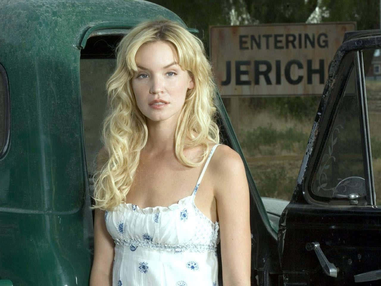 Ashley Scott 桌布 壁紙 — 一位金髮女子身穿白色花卉連衣裙，站在一輛復古綠色卡車旁，附近有一個風化的「Entering Jericho」標誌。