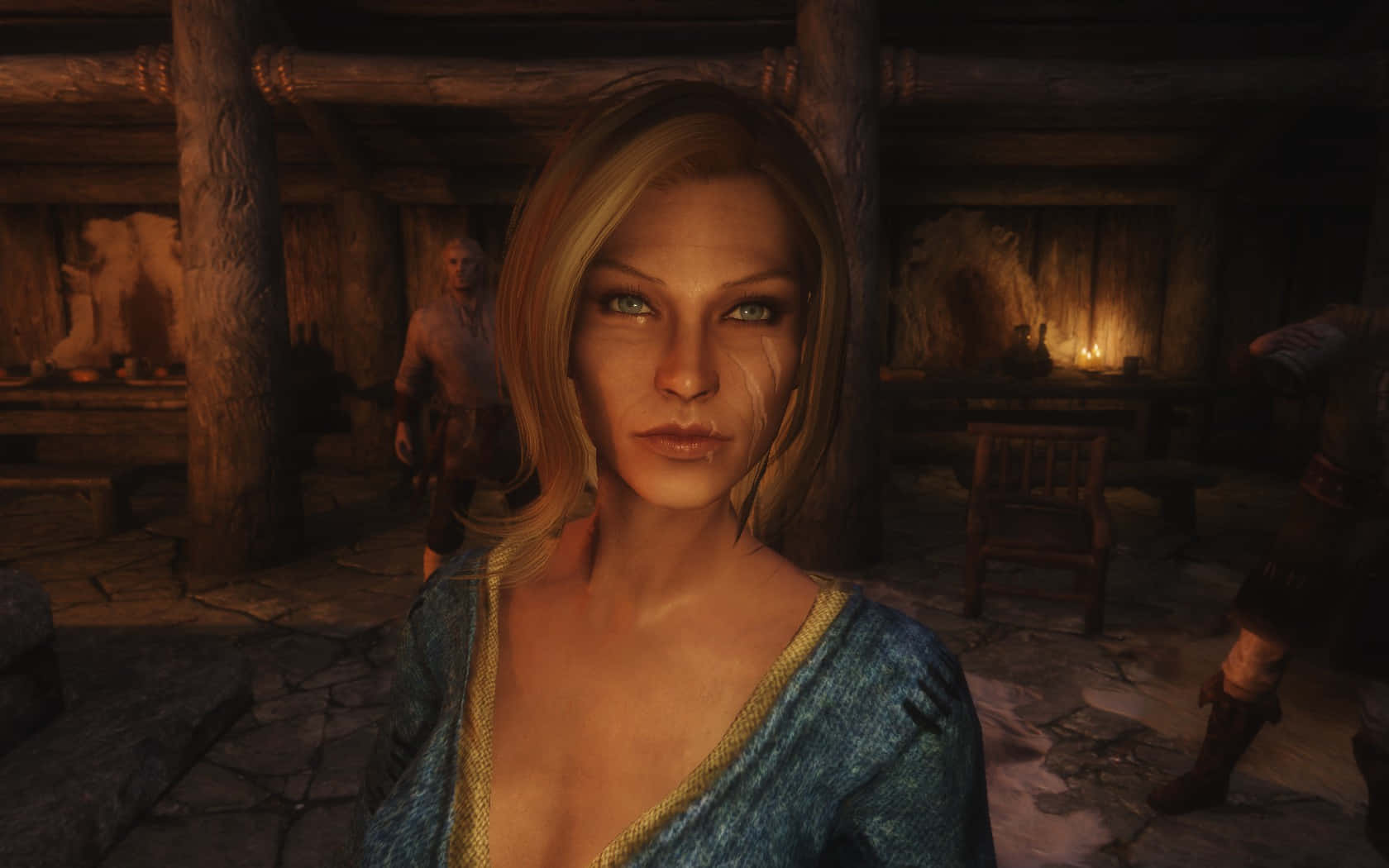 Skyrim Delphine 桌布 壁紙 — 一位金髮女子身穿藍色束腰外衣，在光線昏暗的質樸木製酒館中，石地板和搖曳的燭光下凝視前方。