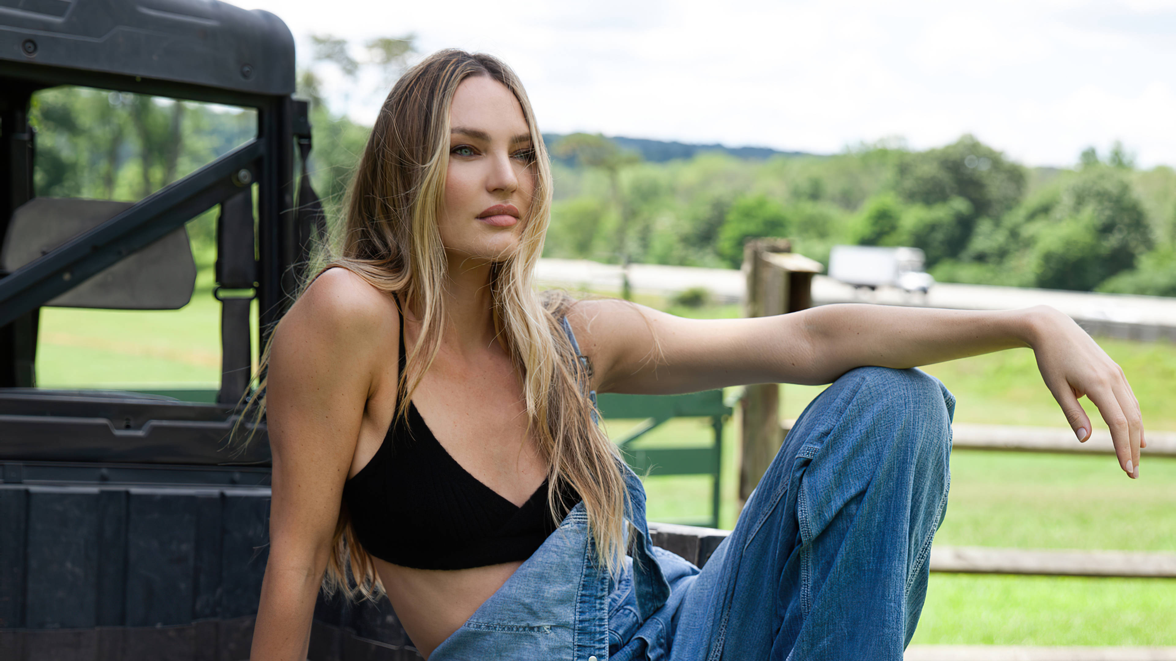 Candice 桌布 壁紙 — 一位金髮女子身穿黑色上衣和牛仔褲，隨意地坐在一輛堅固卡車的後斗上，背景是翠綠的鄉村風光。