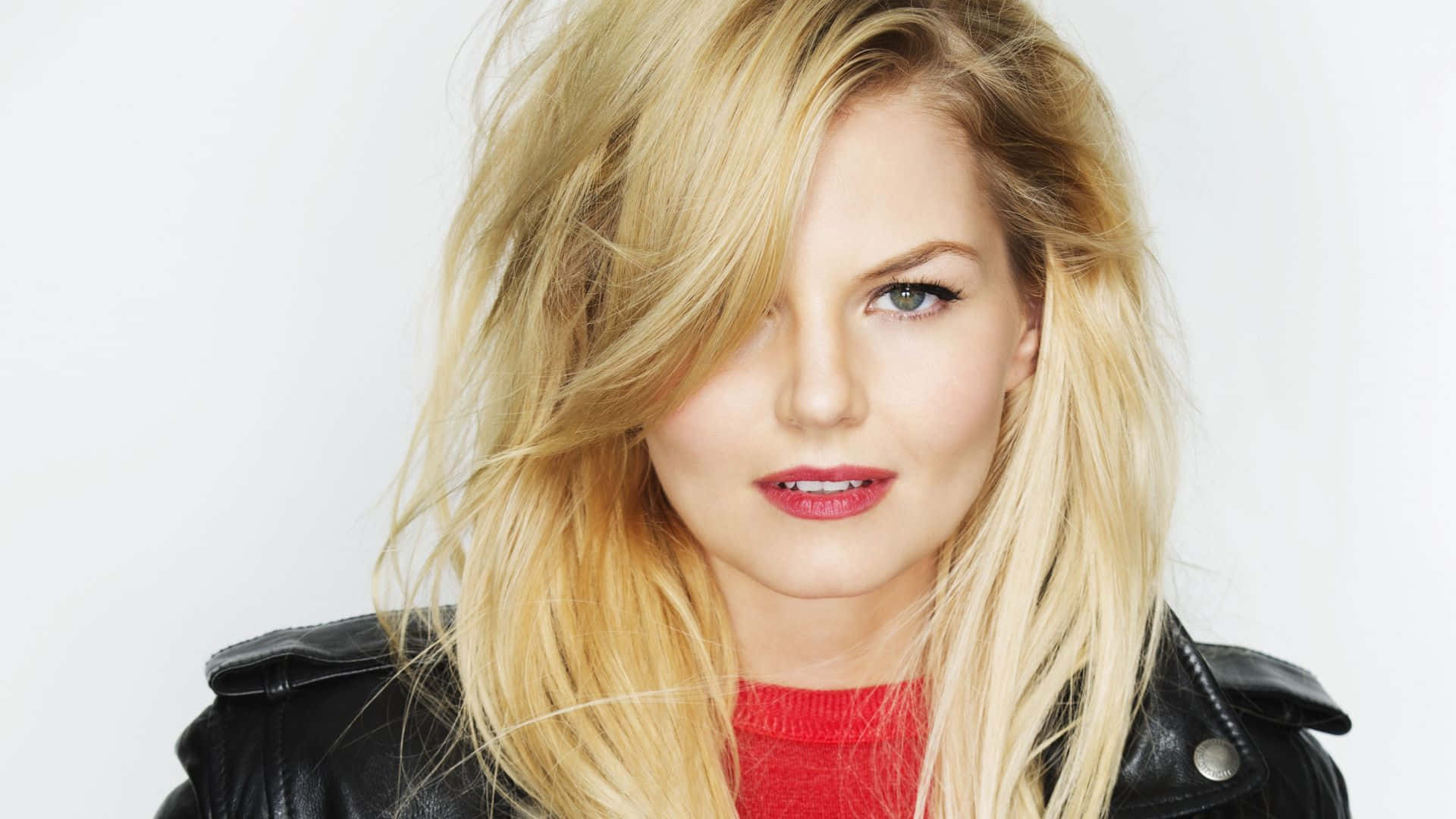 jennifer morrison 桌布 壁紙 — 一位金髮女子頭髮被風吹起，在純白背景前穿著黑色皮夾克內搭紅色毛衣。
