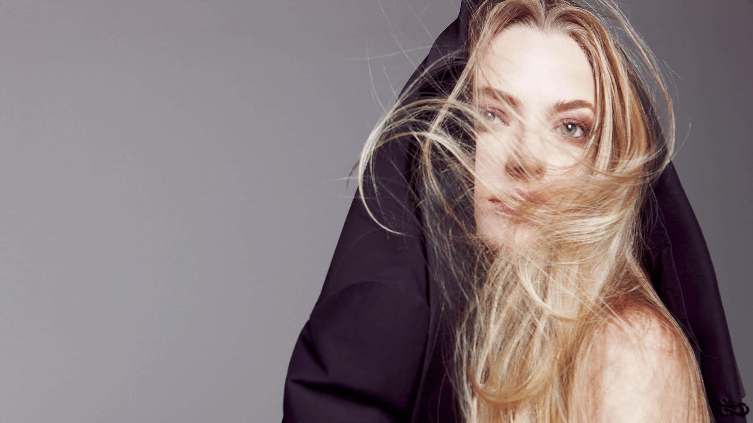 Gemma Ward 桌布 壁紙 — 一位金髮女子頭髮被風吹起，披著黑色連帽衫，在灰色攝影棚背景下凝視著鏡頭。