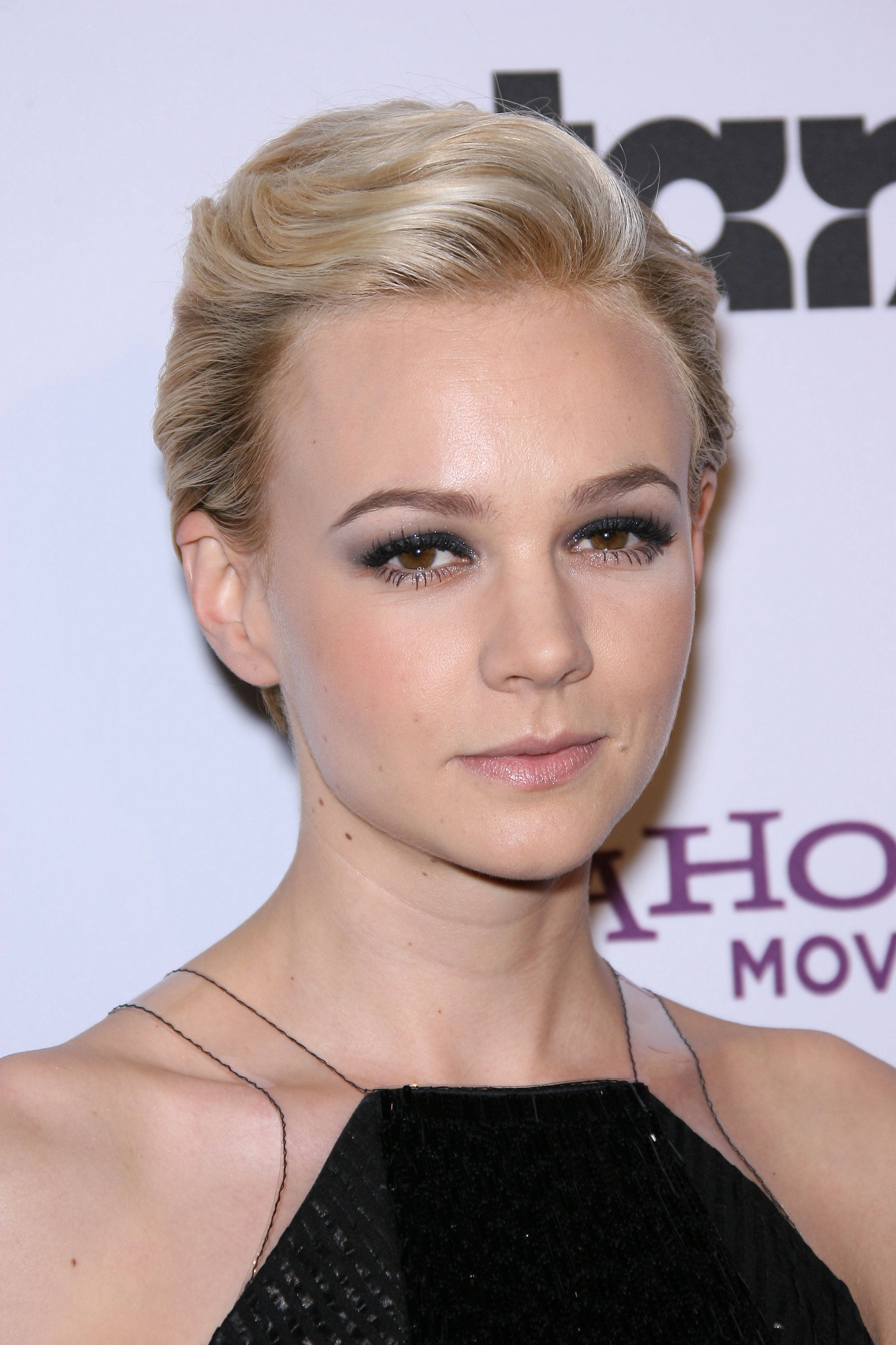 Carey Mulligan 桌布 壁紙 — 一位金髮女性在活動中穿著黑色連衣裙，擁有造型頭髮和深色眼線的特寫肖像。