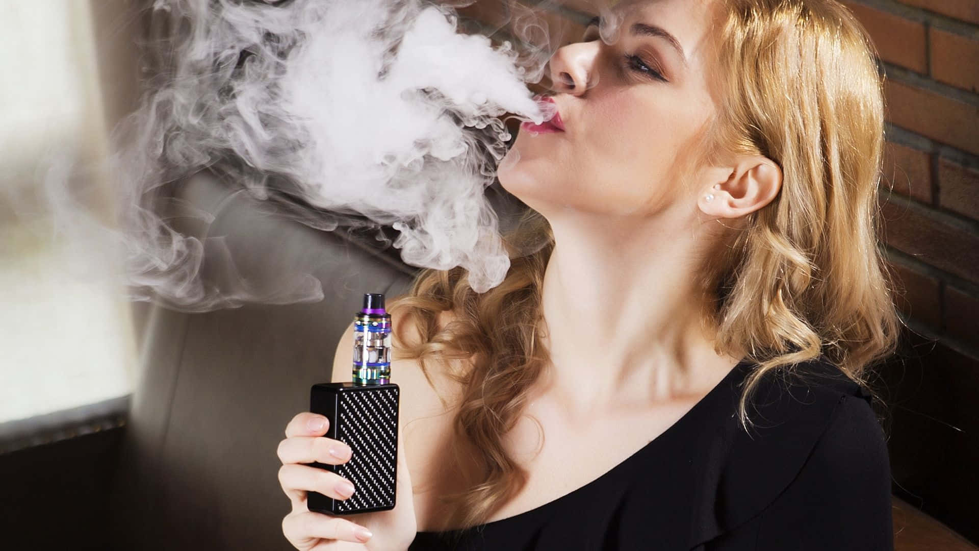 抽菸 桌布 壁紙 — 一位金髮女性在磚牆背景下呼出一團濃厚的蒸氣，同時手持電子煙裝置。