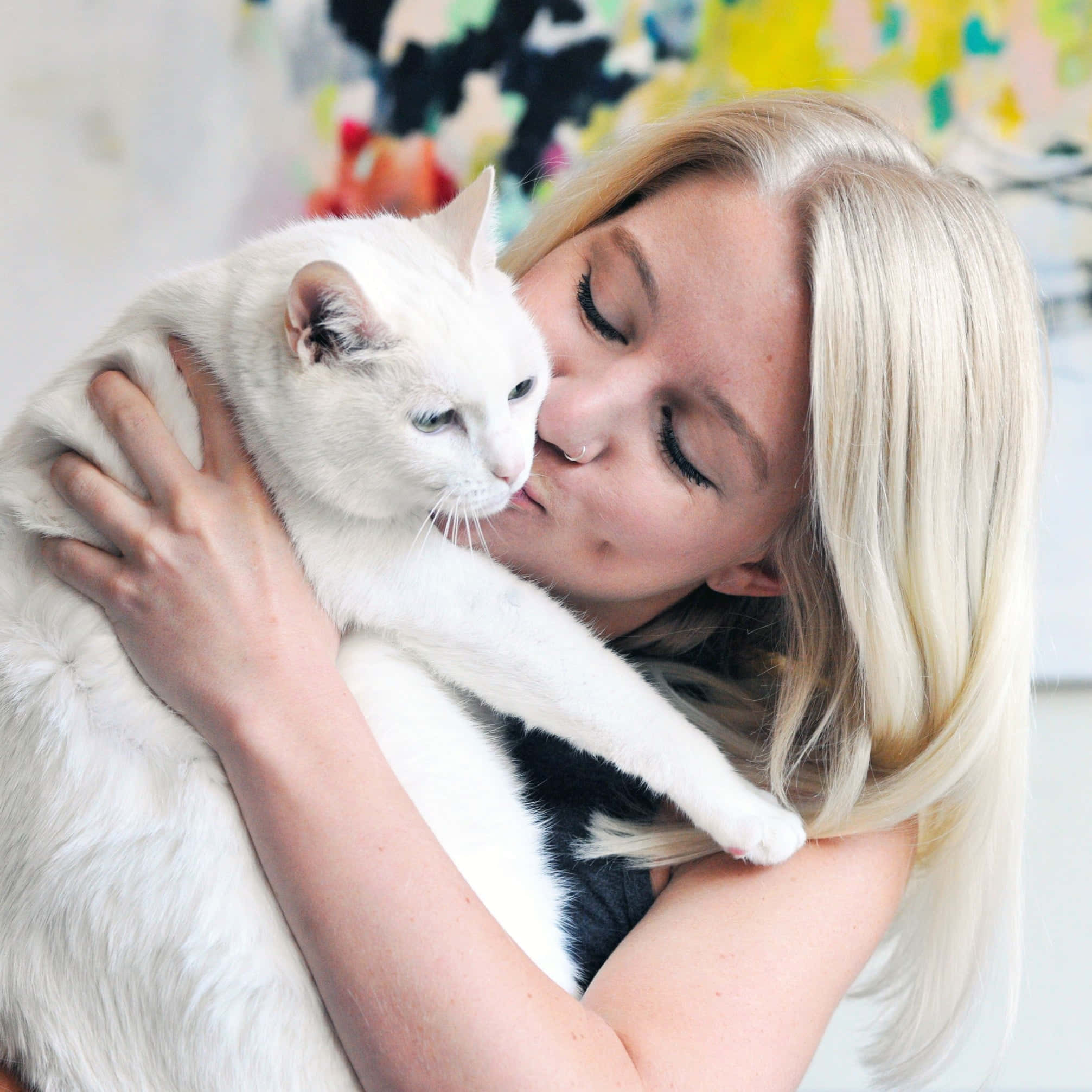 Beautiful Cats 桌布 壁紙 — 一位金髮女性在身後有抽象藝術的柔和光線房間中，溫柔地親吻她抱緊的白貓。