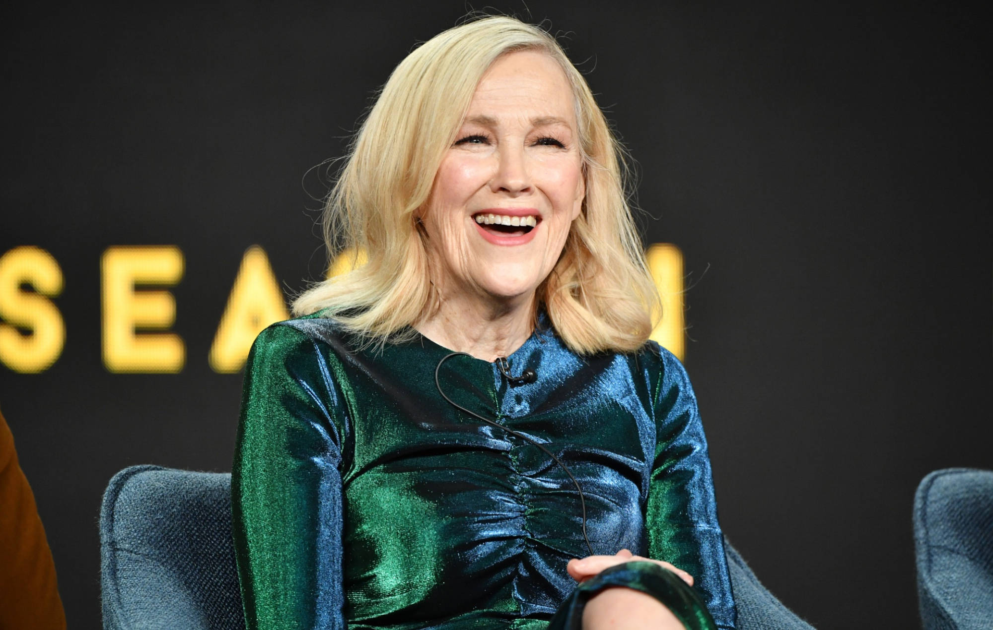 Celebrity 桌布 壁紙 — 一位金髮女性坐在椅子上，穿著閃閃發光的綠色連衣裙，開心地大笑。