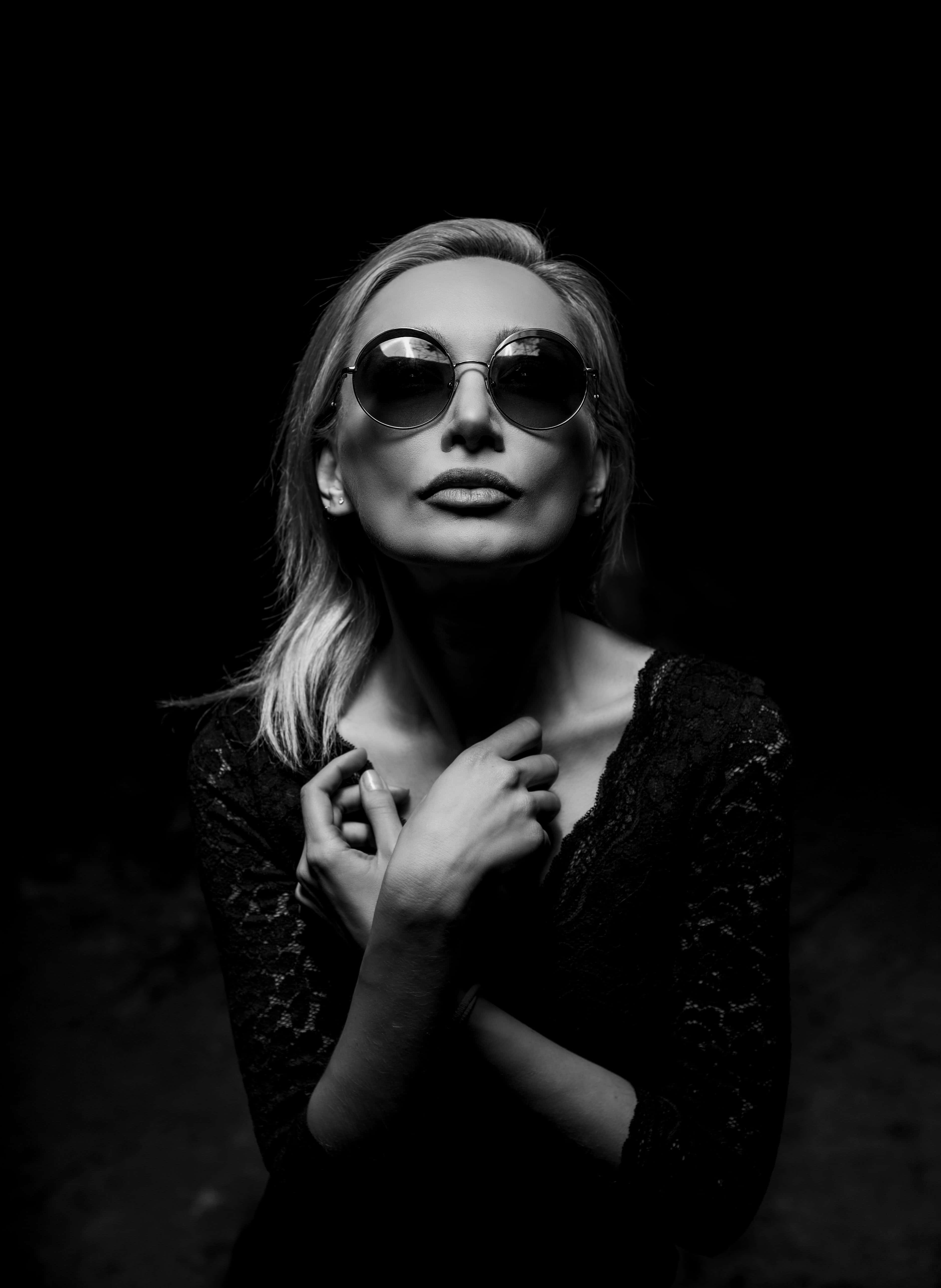 女孩 桌布 壁紙 — 一位金髮女性戴著圓形太陽眼鏡和蕾絲上衣，背景為純黑色。