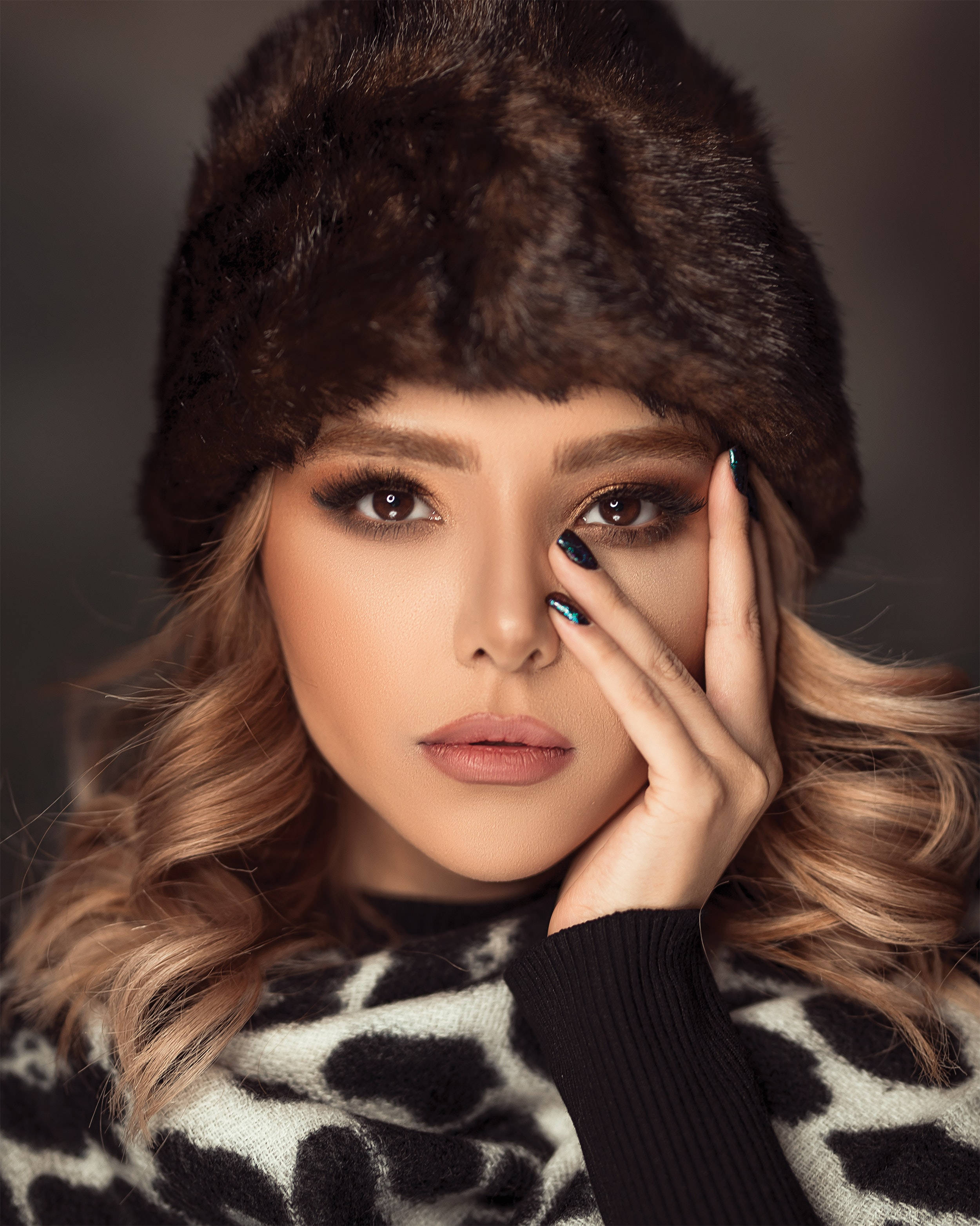fur 桌布 壁紙 — 一位金髮女性戴著棕色毛帽和豹紋圍巾，用塗了指甲油的手觸摸臉部。