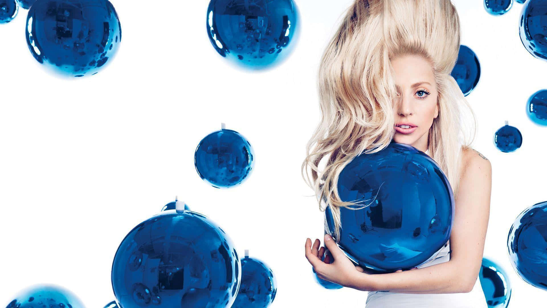 Lady Gaga 桌布 壁紙 — 一位金髮女性手持一個大型藍色鏡面球，周圍漂浮著迪斯可球，背景為純白色。