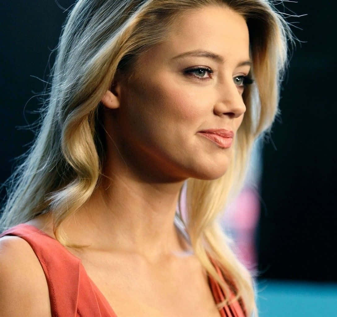 Amber Heard 桌布 壁紙 — 一位金髮女性的特寫肖像，光線柔和，面帶溫柔微笑，身穿珊瑚色上衣。
