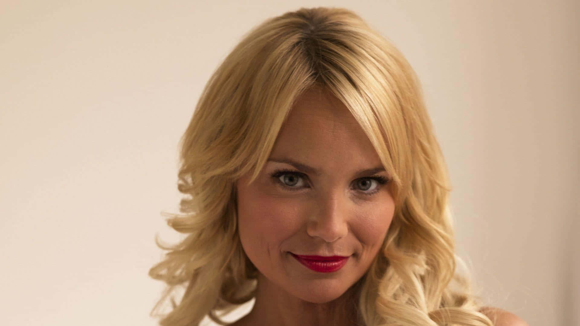 kristin chenoweth 桌布 壁紙 — 一位金髮女性的特寫肖像，她有鮮紅色的嘴唇，在純米色背景前輕輕微笑。