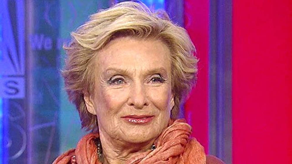 Celebrity 桌布 壁紙 — 一位金髮女性的特寫肖像，帶著溫暖笑容，戴著橙色圍巾，背景是充滿活力的紅色和藍色攝影棚。