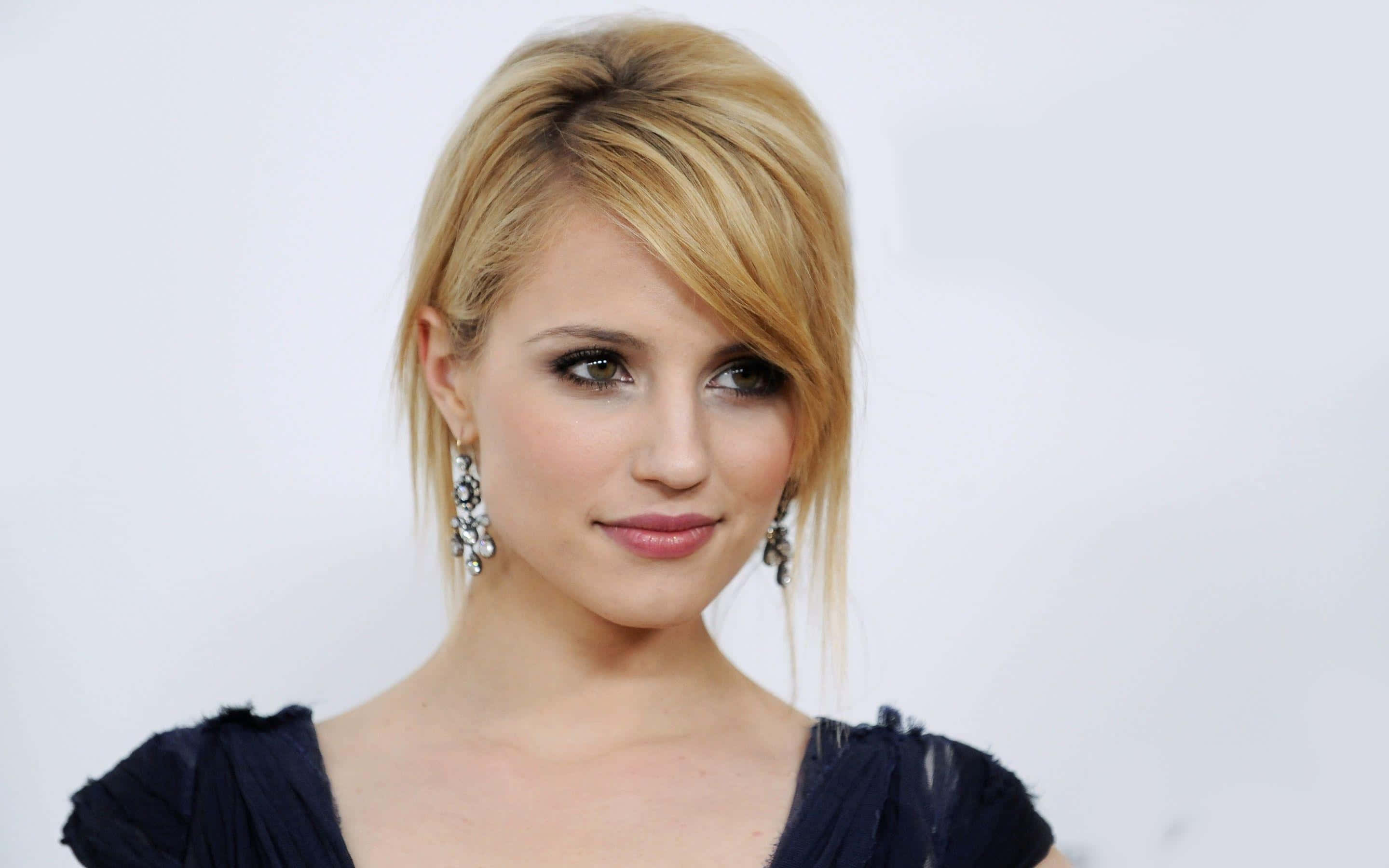dianna agron 桌布 壁紙 — 一位金髮女性的特寫肖像，戴著優雅的垂墜耳環和深藍色上衣，背景為純白色。