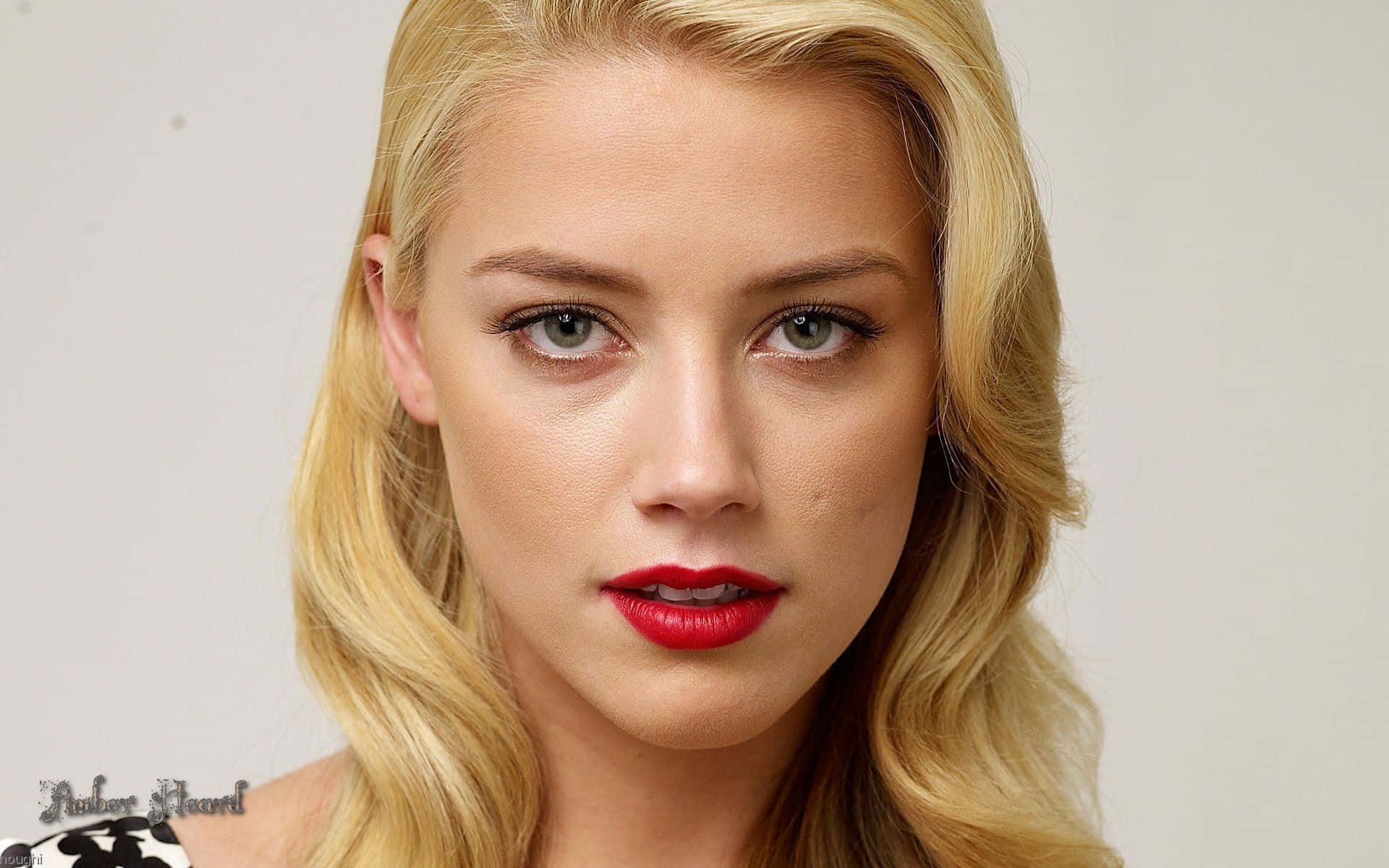 Amber Heard 桌布 壁紙 — 一位金髮女性的特寫肖像，擁有引人注目的綠色眼睛和鮮豔的紅唇，背景為純色。