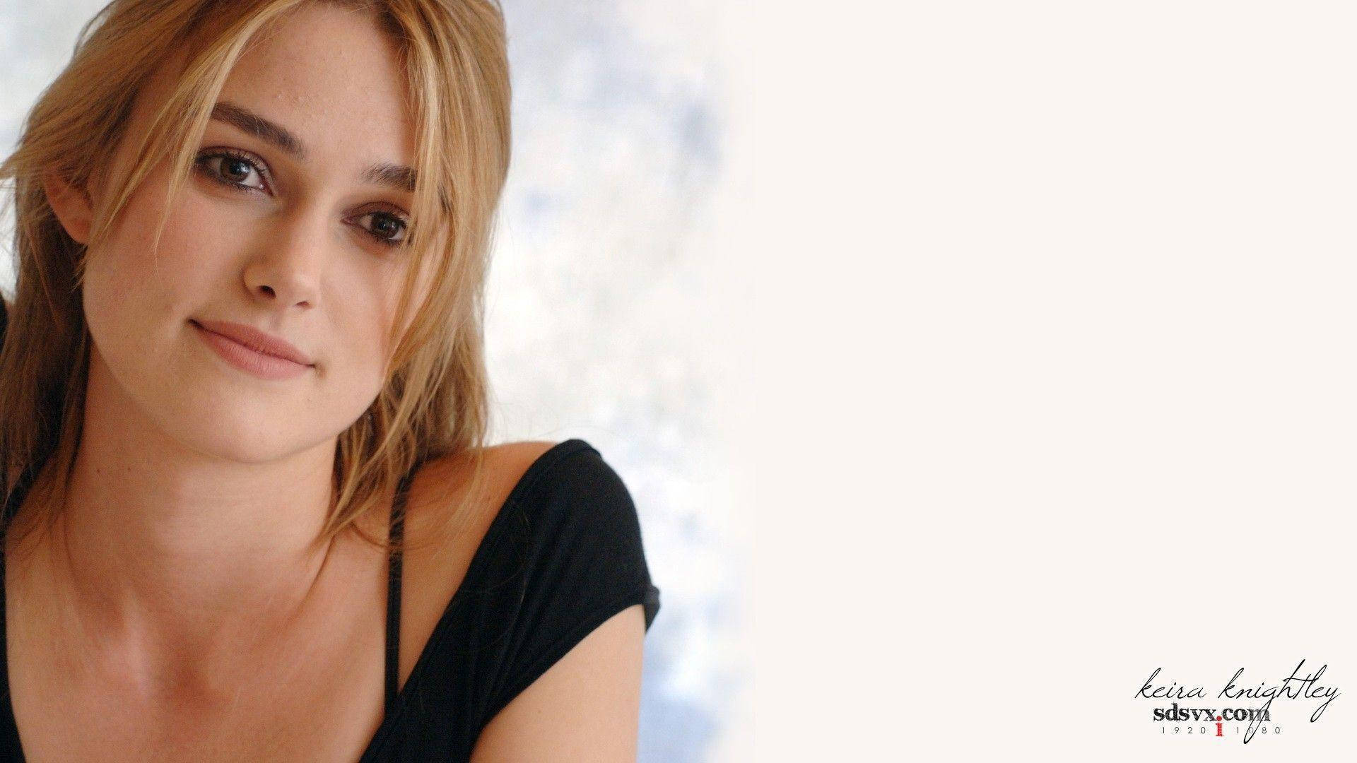 Keira Knightley 桌布 壁紙 — 一位金髮女性的近距離肖像，帶著溫柔的微笑，身穿黑色上衣，背景柔和模糊。