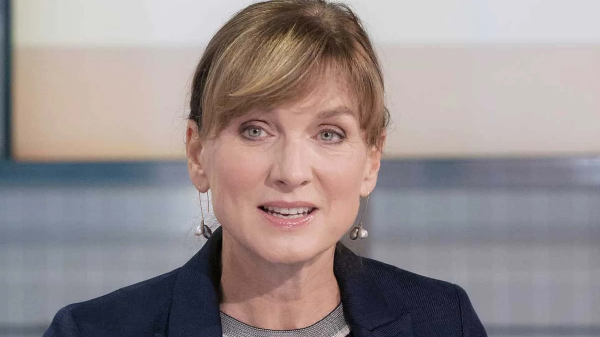 Fiona Bruce 桌布 壁紙 — 一位金髮女性的近距離肖像，穿著深色西裝外套和珍珠耳環，背景模糊。
