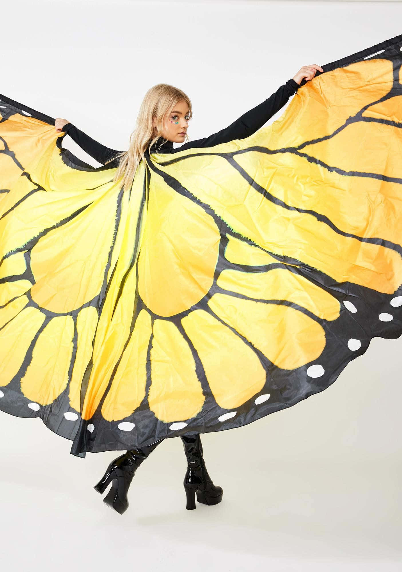 Butterfly Wing Dress 桌布 壁紙 — 一位金髮女性穿著大型黃黑相間的帝王蝶服裝，背景為純白色。