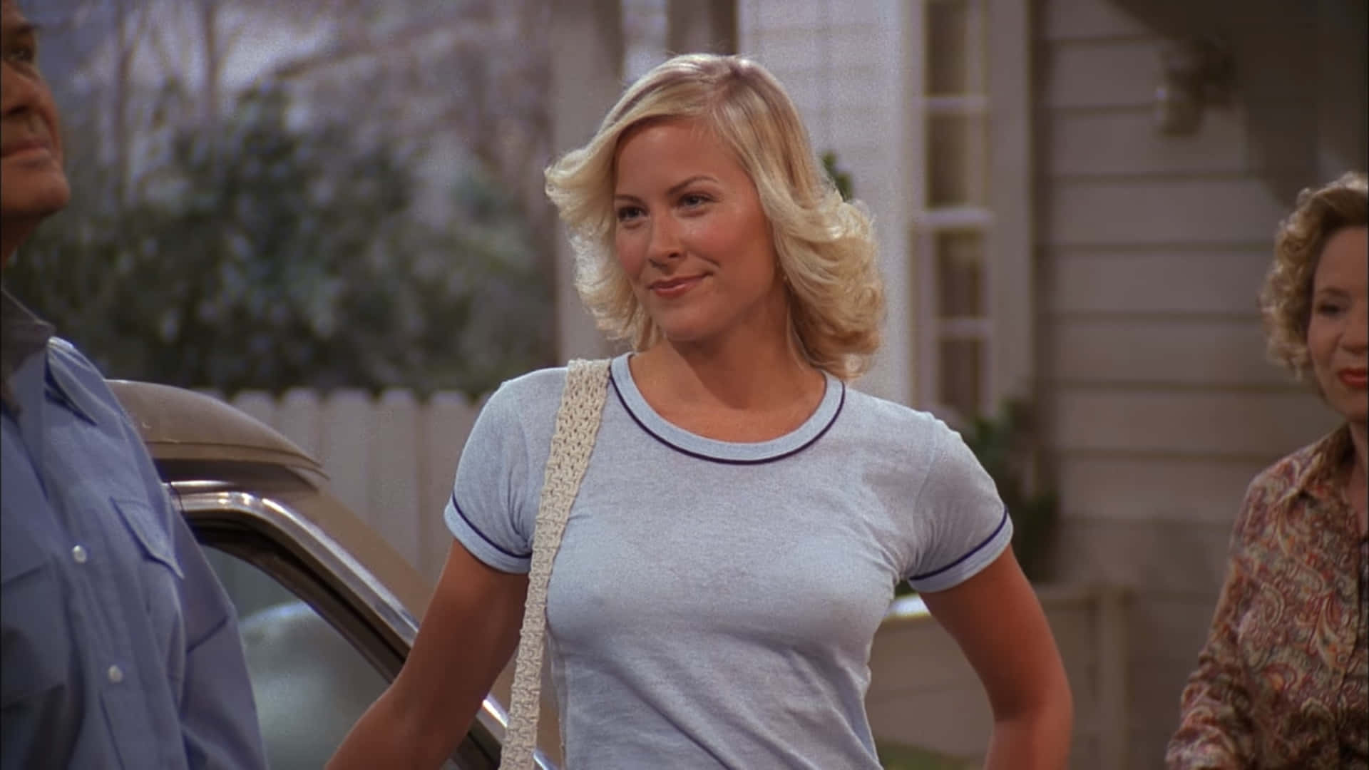 Brittany Daniel 桌布 壁紙 — 一位金髮女性穿著淺藍色T恤，微笑著站在一輛車旁，附近還有另外兩個人。