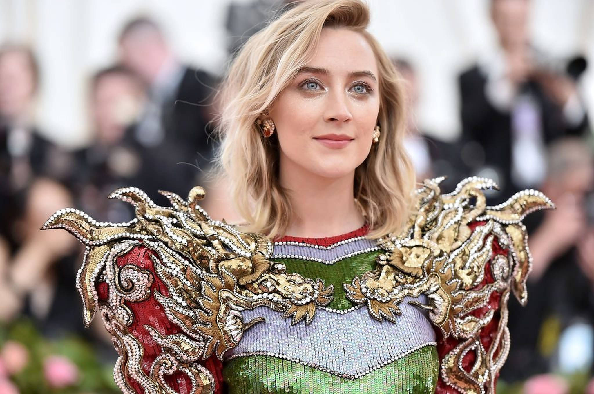 Saoirse Ronan 桌布 壁紙 — 一位金髮女性穿著華麗的紅、綠、金色珠飾長袍，肩部裝飾誇張，出席一場魅力四射的活動。