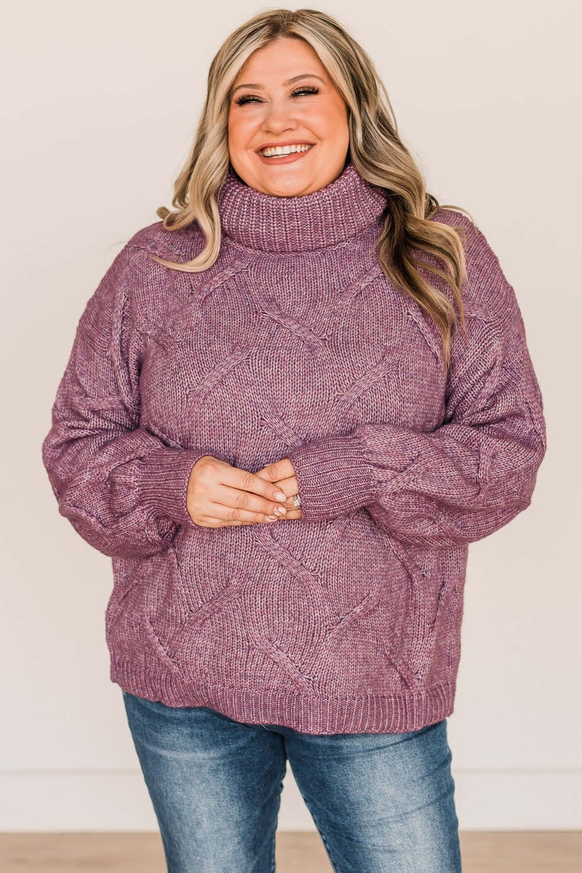 Purple Turtle-neck Sweater 桌布 壁紙 — 一位金髮女性穿著質感紫色高領毛衣和藍色牛仔褲，在素色背景前溫暖微笑。