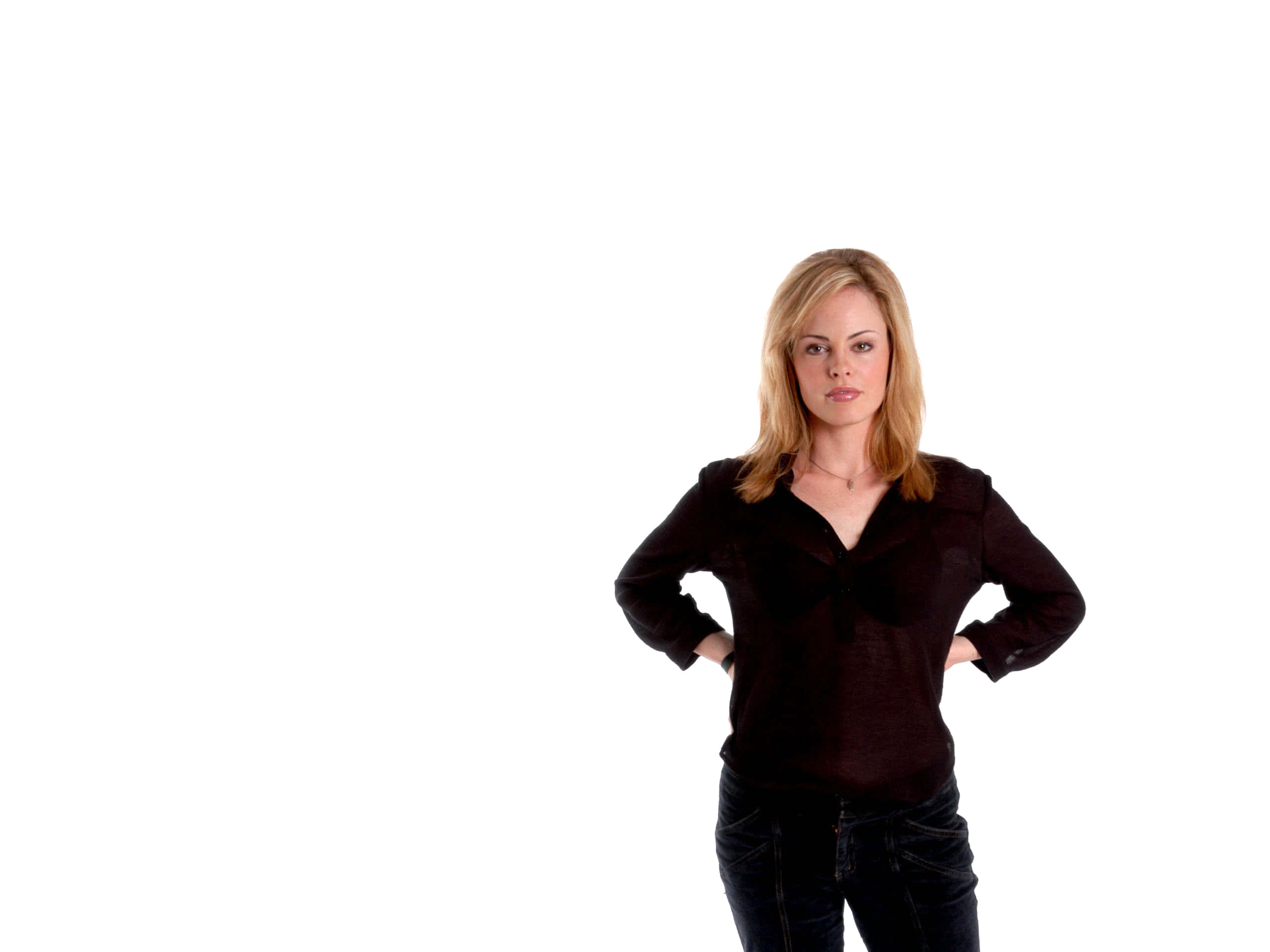Chandra West 桌布 壁紙 — 一位金髮女性自信地站在純白背景前，穿著深色襯衫和牛仔褲。
